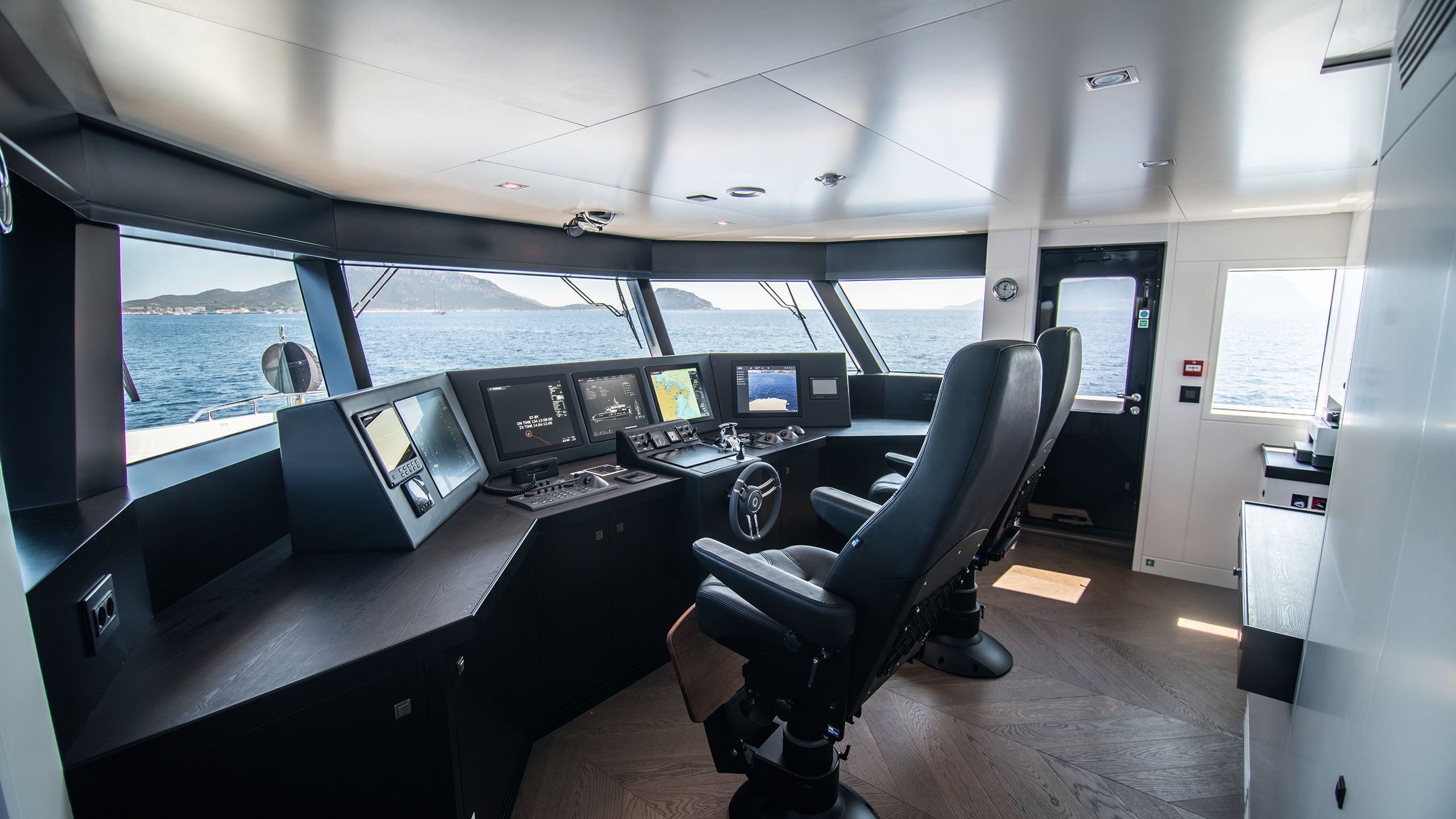 Inside the wheelhouse - there are two chairs in black leather facing a desk of controls and screens