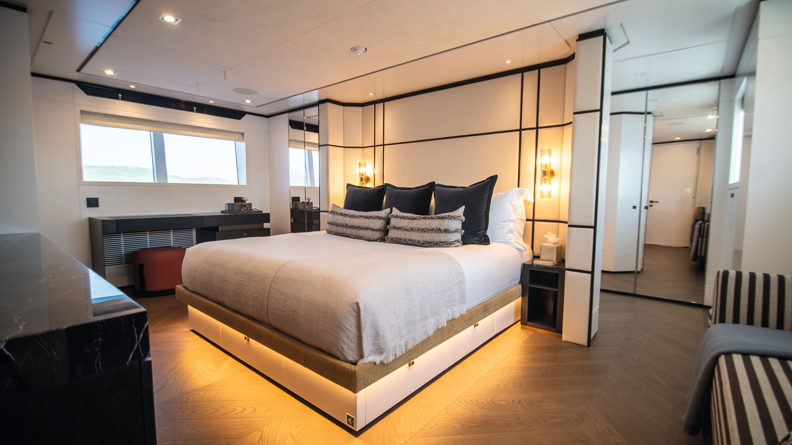 A cabin with bed in the centre that has white sheets, neutral throw and blue cushions