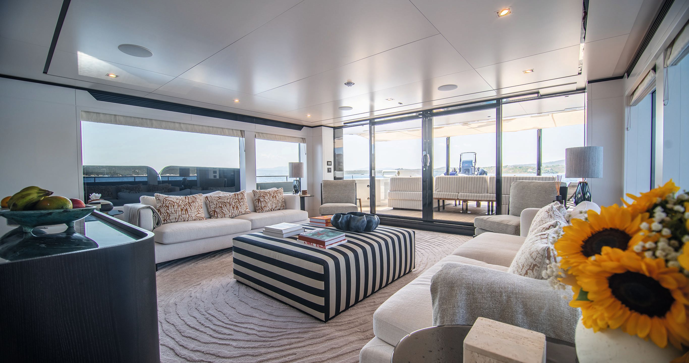A lounge area with two oblong sofas facing each other. In the centre is a striped padded footrest doubling as a table