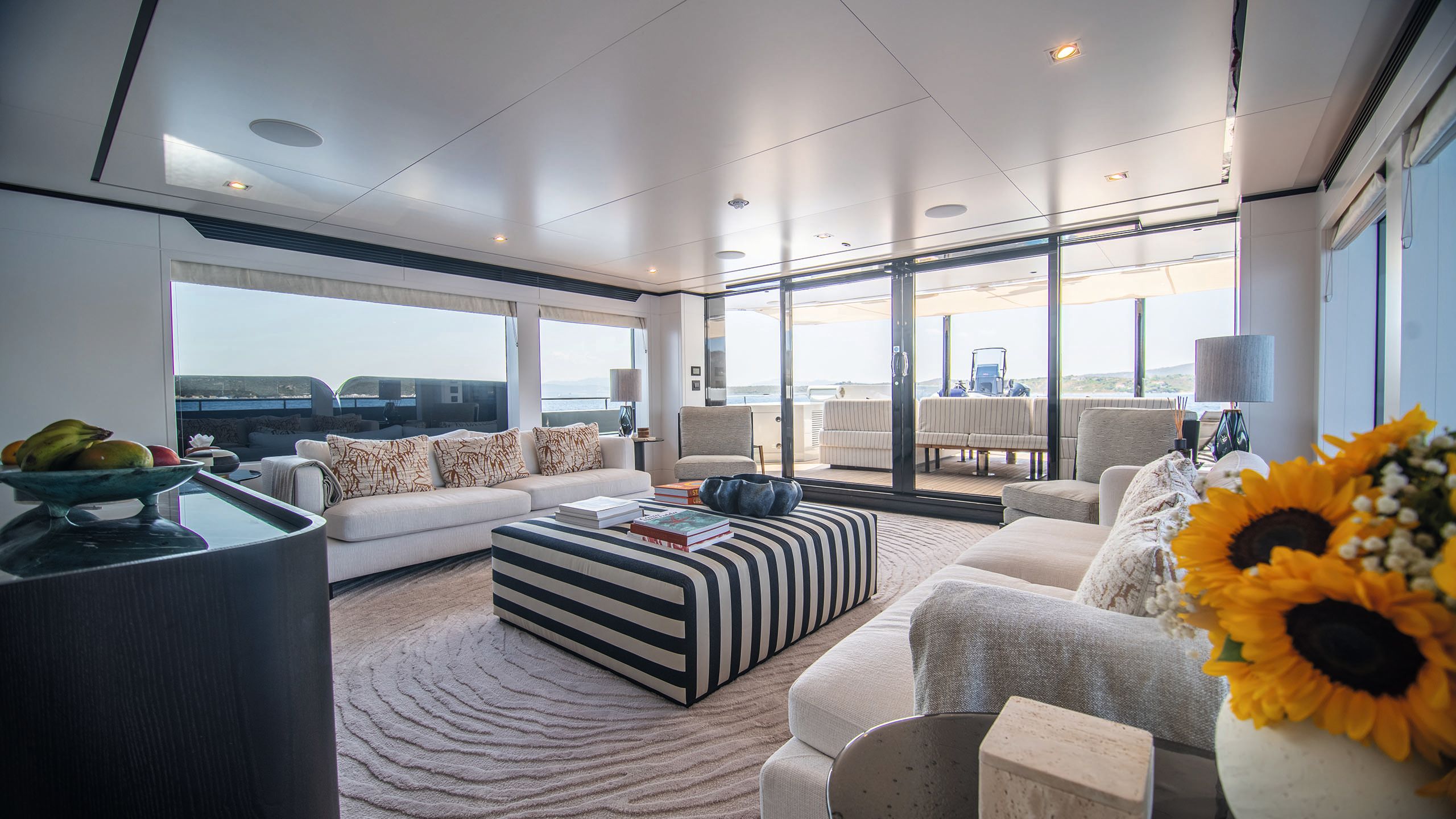 A lounge area with two oblong sofas facing each other. In the centre is a striped padded footrest doubling as a table