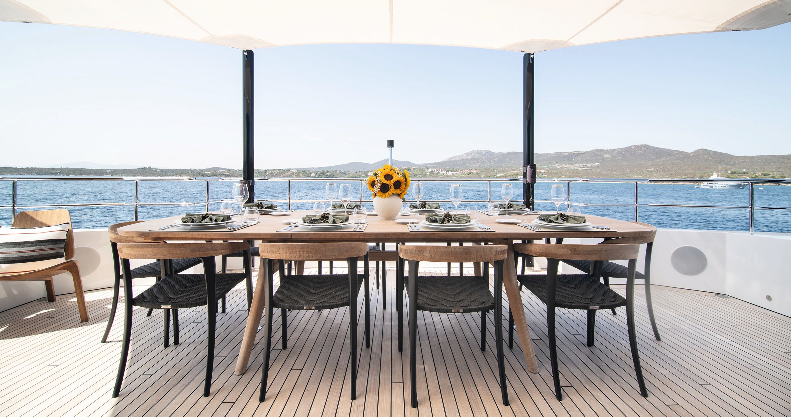 Wood dining table and chairs set for 10 with a vase of sunflowers at the centre and a white canopy overhead