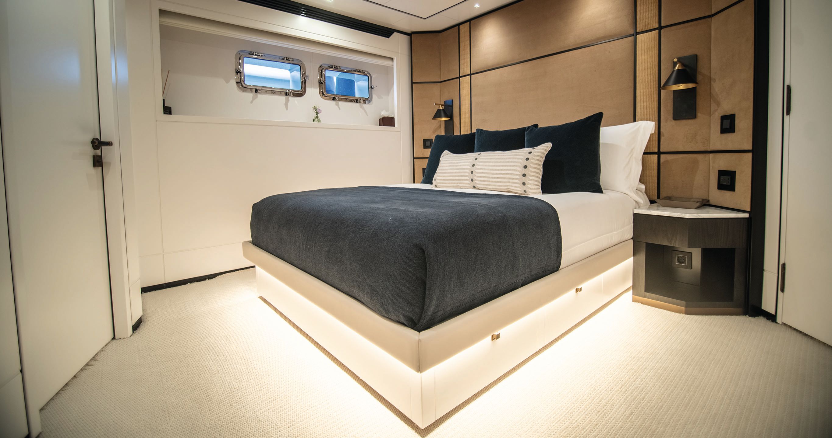 A cabin with double bed at the centre. It has white linens with a dark throw and cushions