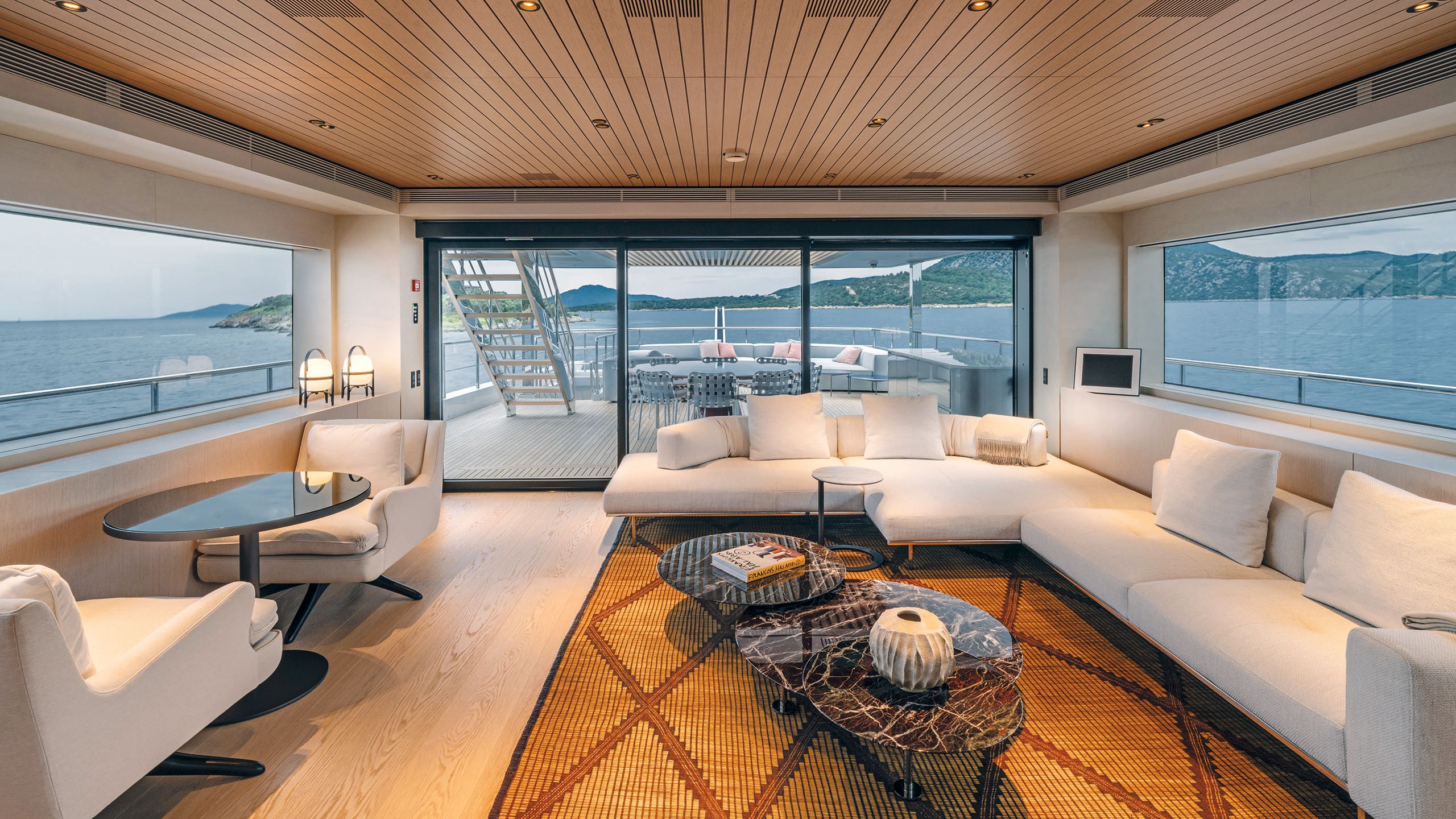 Large L-shaped sofa in cream with two arm chairs opposite with a table in between. Three marble-effect nestled round tables are in front of the couch