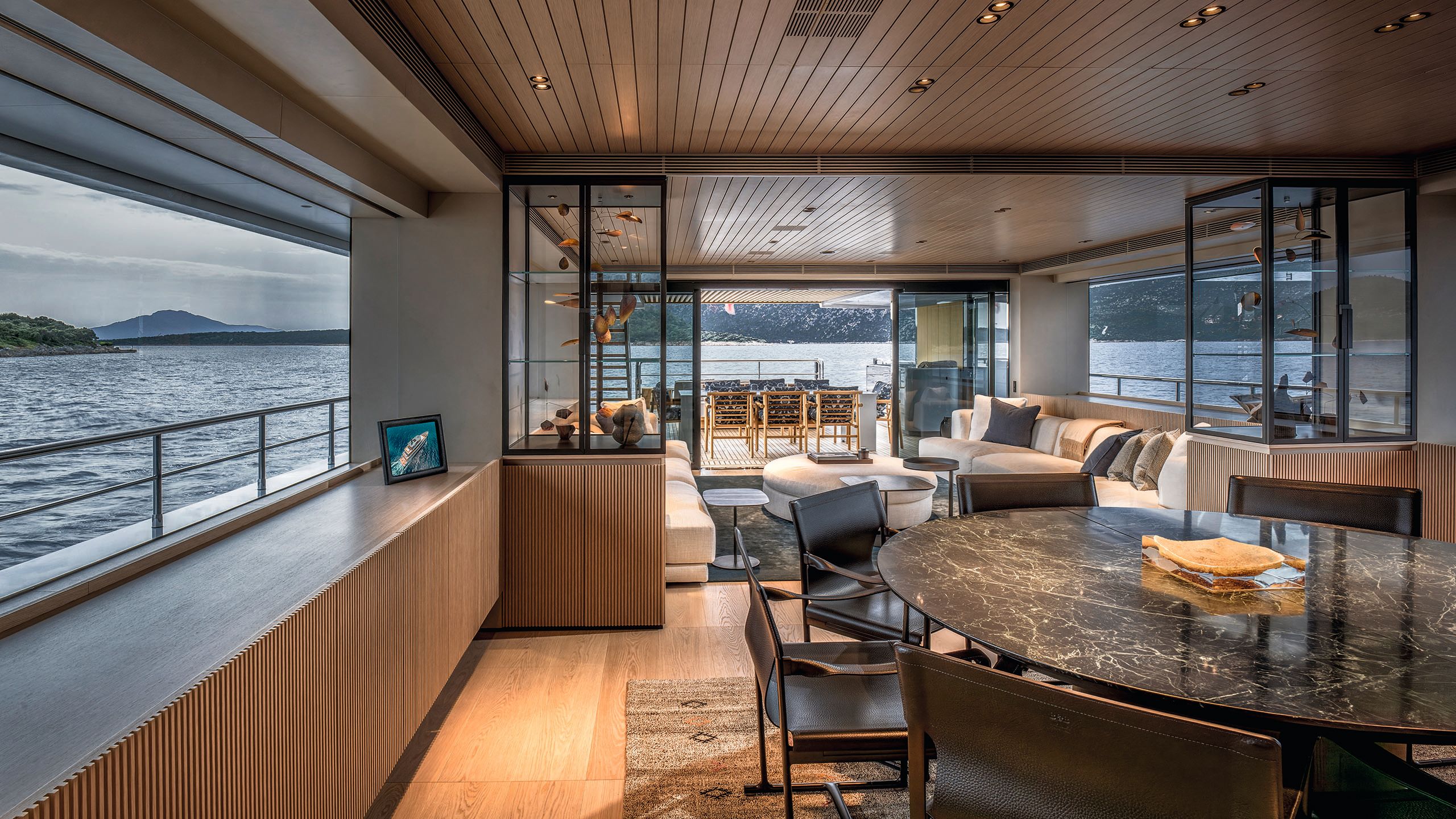 The main saloon has a large marble-effect black table with chairs surrounding, soft seats to the rear and glass cabinets holding artworks