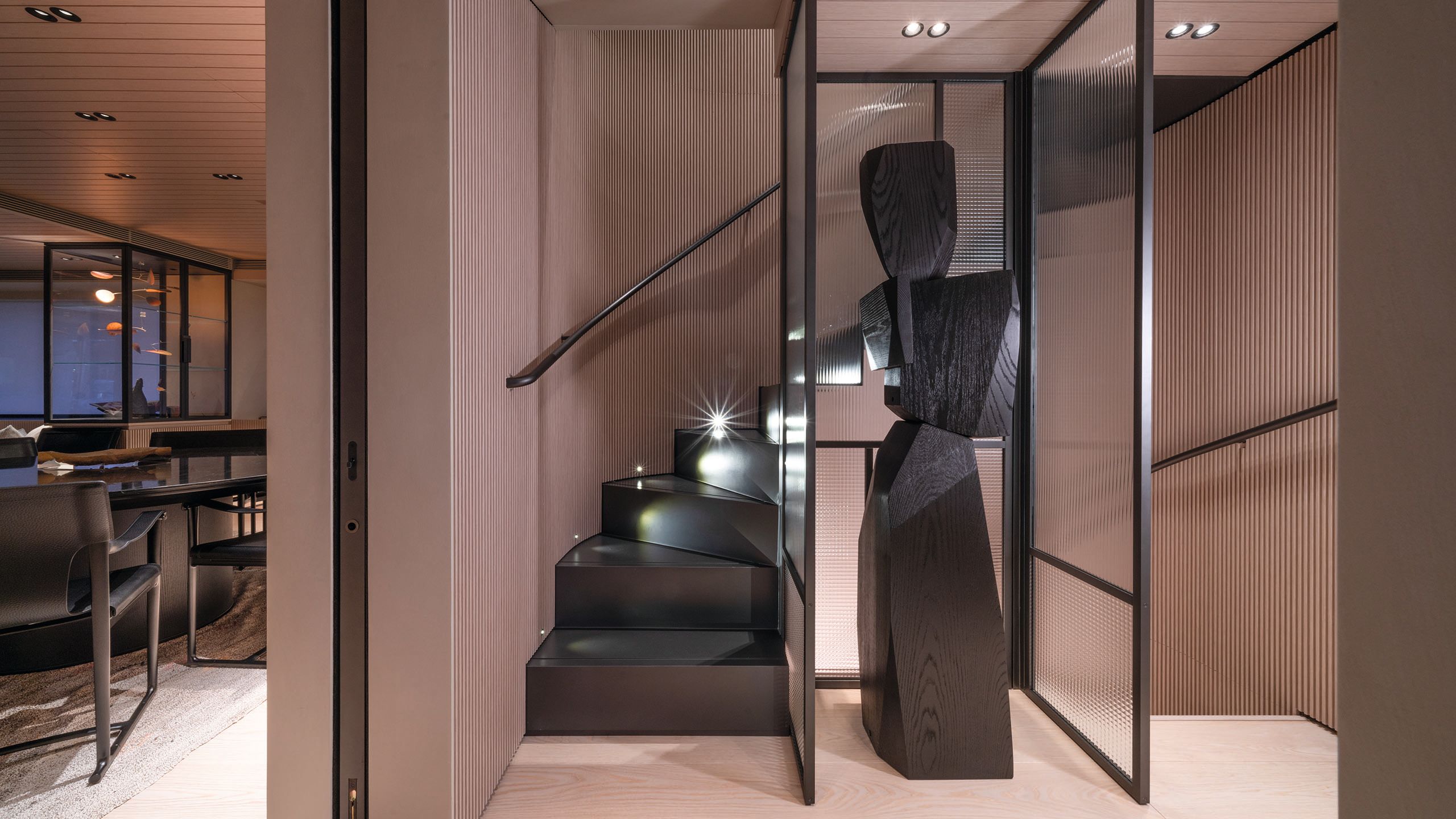Slender black staircase and abstract artwork of a statue to the side. The walls are dusky pink and ribbed