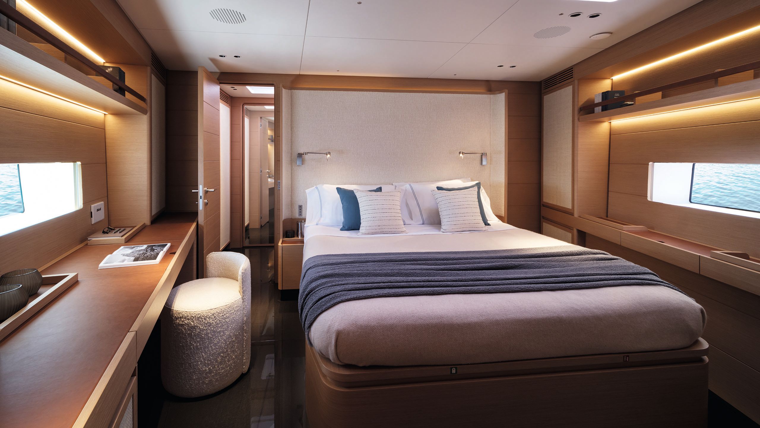 A bed in the centre of a cabin with a blue throw and white linens. A small white boucle chair is in front of a longer counter