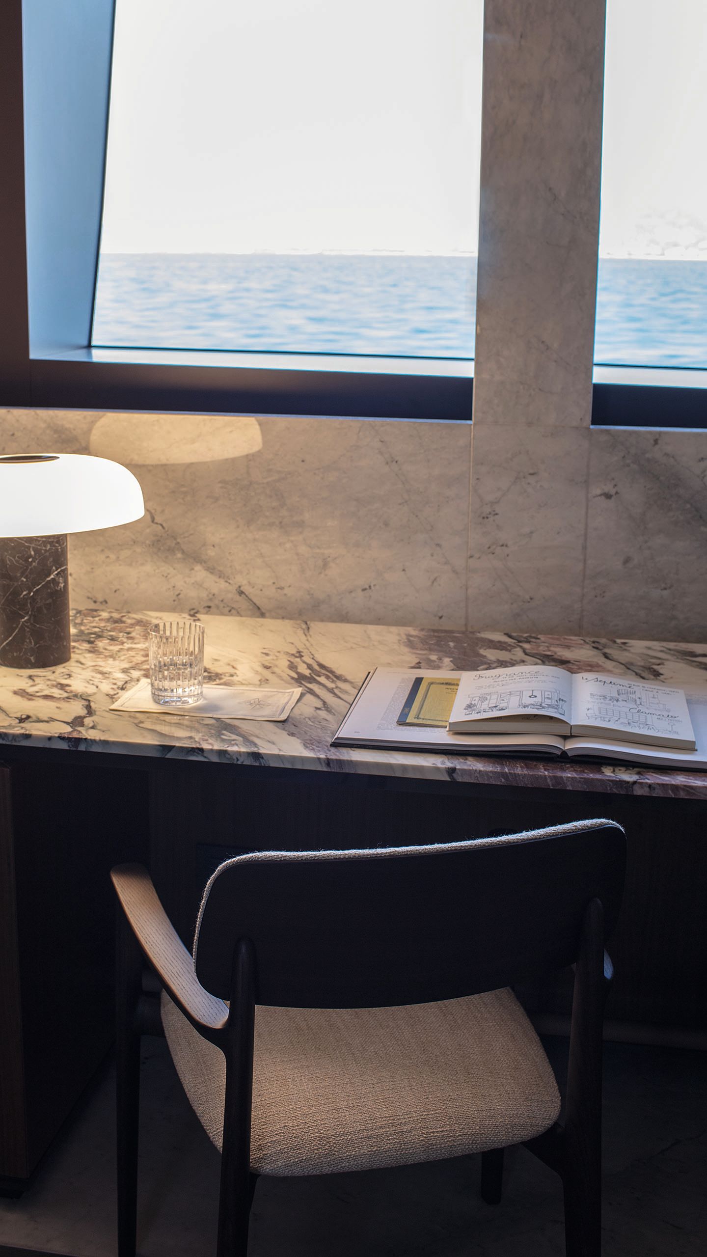 A marble desk and chair in front of a window looking out to sea
