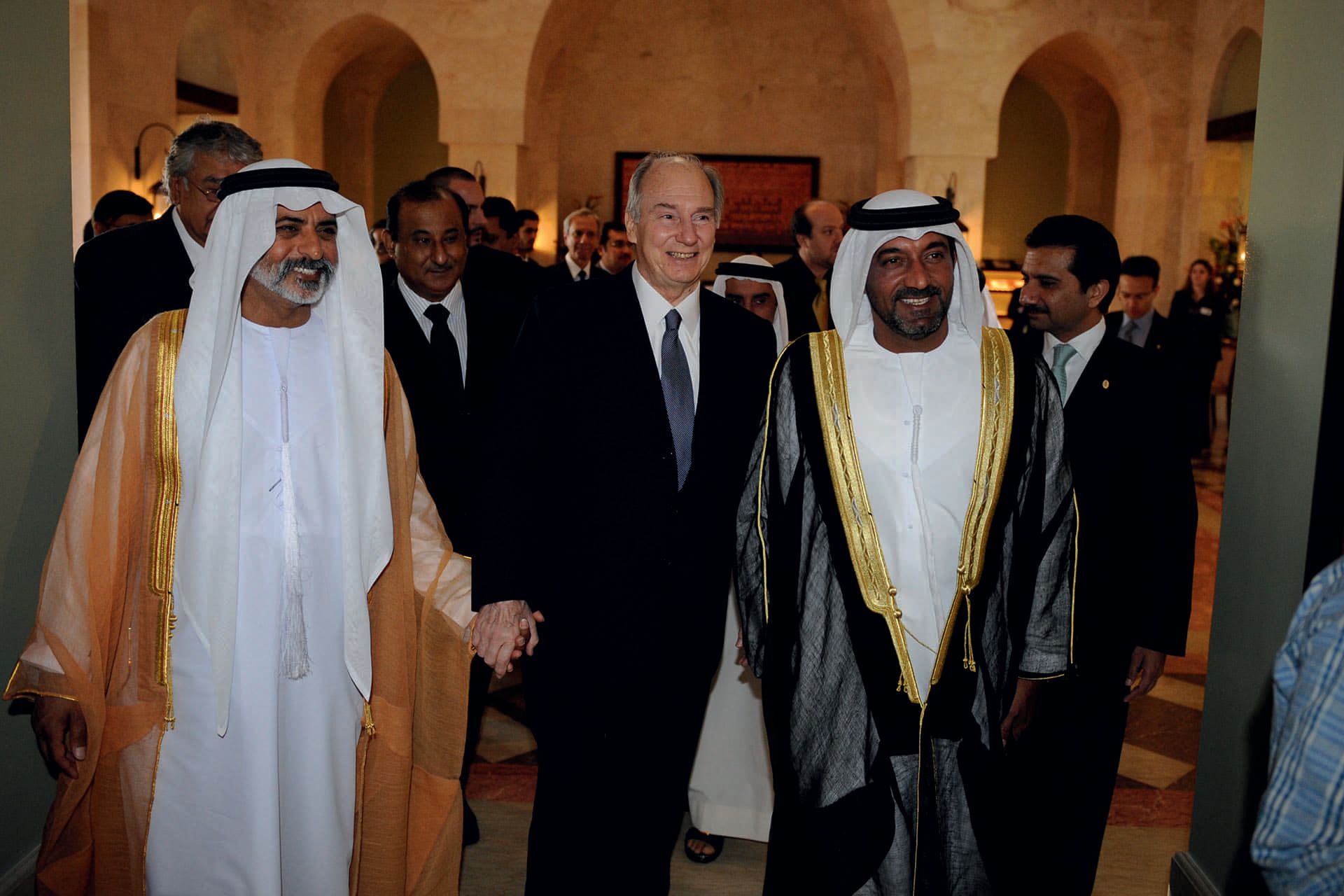 Aga Khan flanked by two men, he is wearing a suit while the others are wearing thobes
