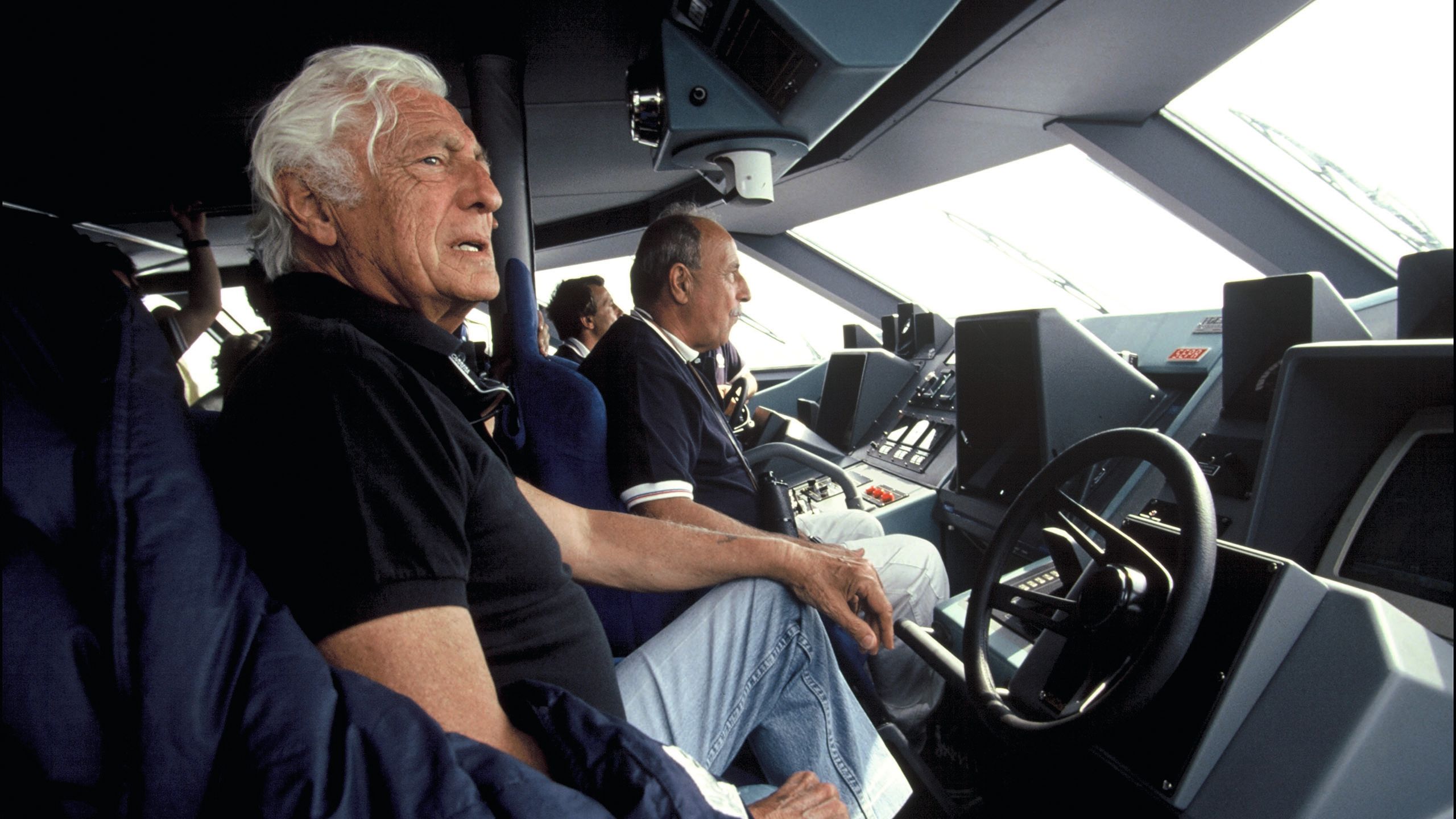 Three men sitting at the helm of a vessel, in the centre is Khan