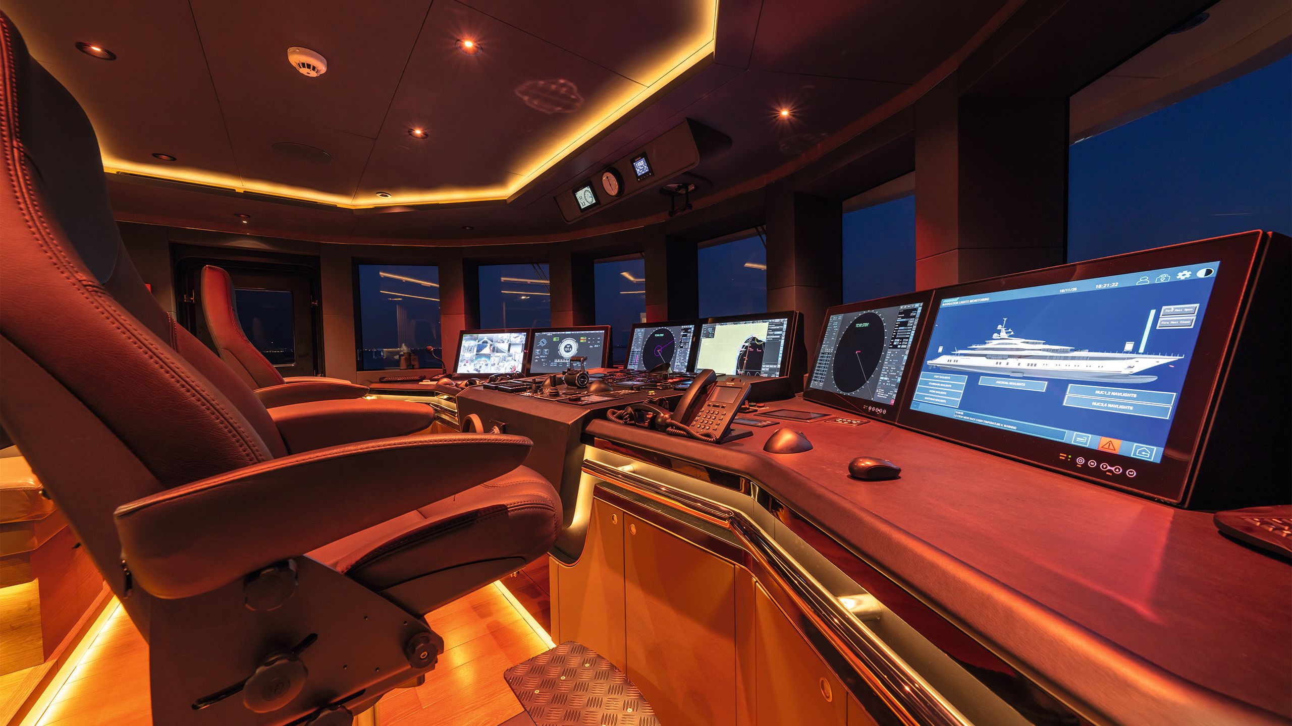 Inside the wheelhouse - there are two leather chairs facing a desk of controls and screens. The lighting is red