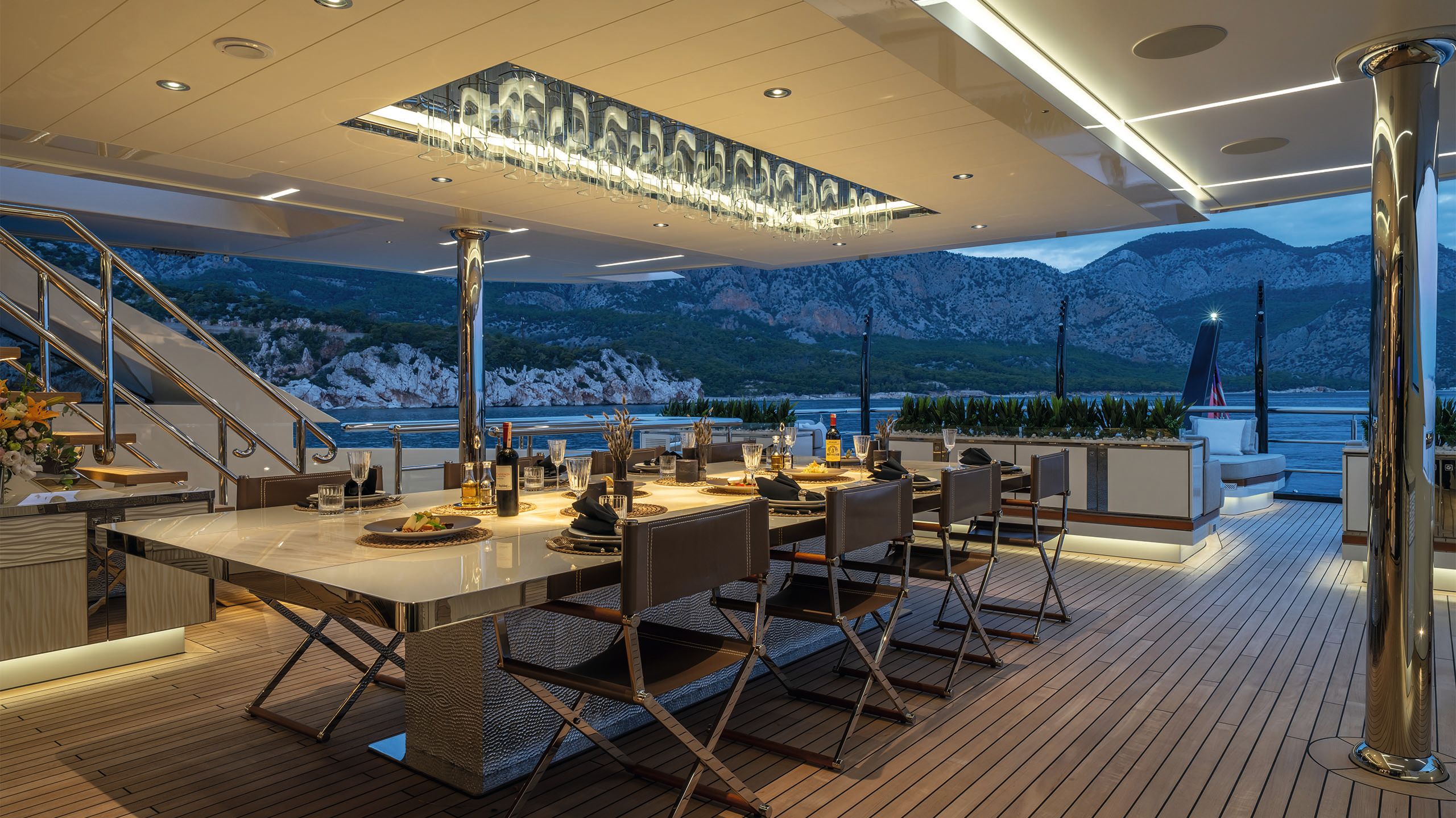 Long, marble-topped dining table on a covered deck. It's set with plates of food, wine glasses and two bottle of red wine
