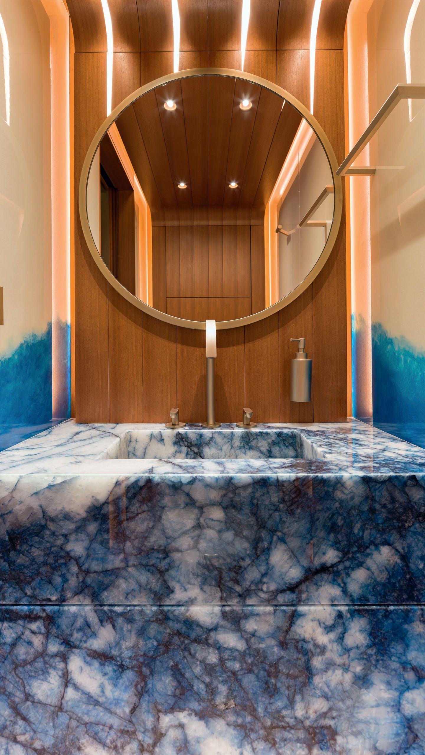 A blue marble pedestal with sink inlaid. Above is a teak splashback and circular mirror