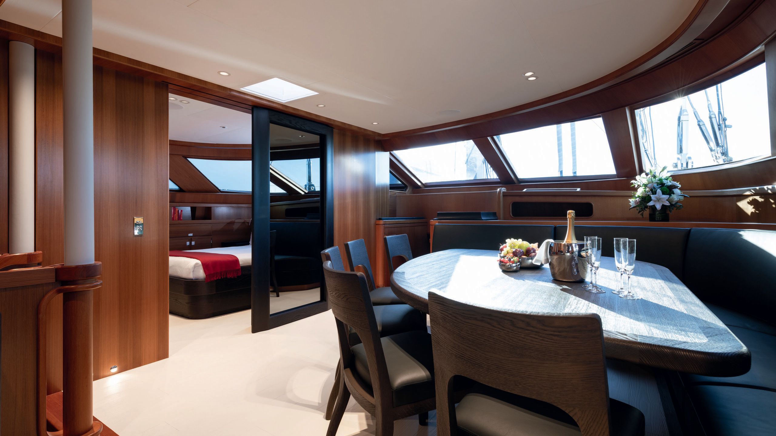 A dining table with chairs around it and a bottle of champagne with glasses. To the left is a sliding glass door with a bed behind