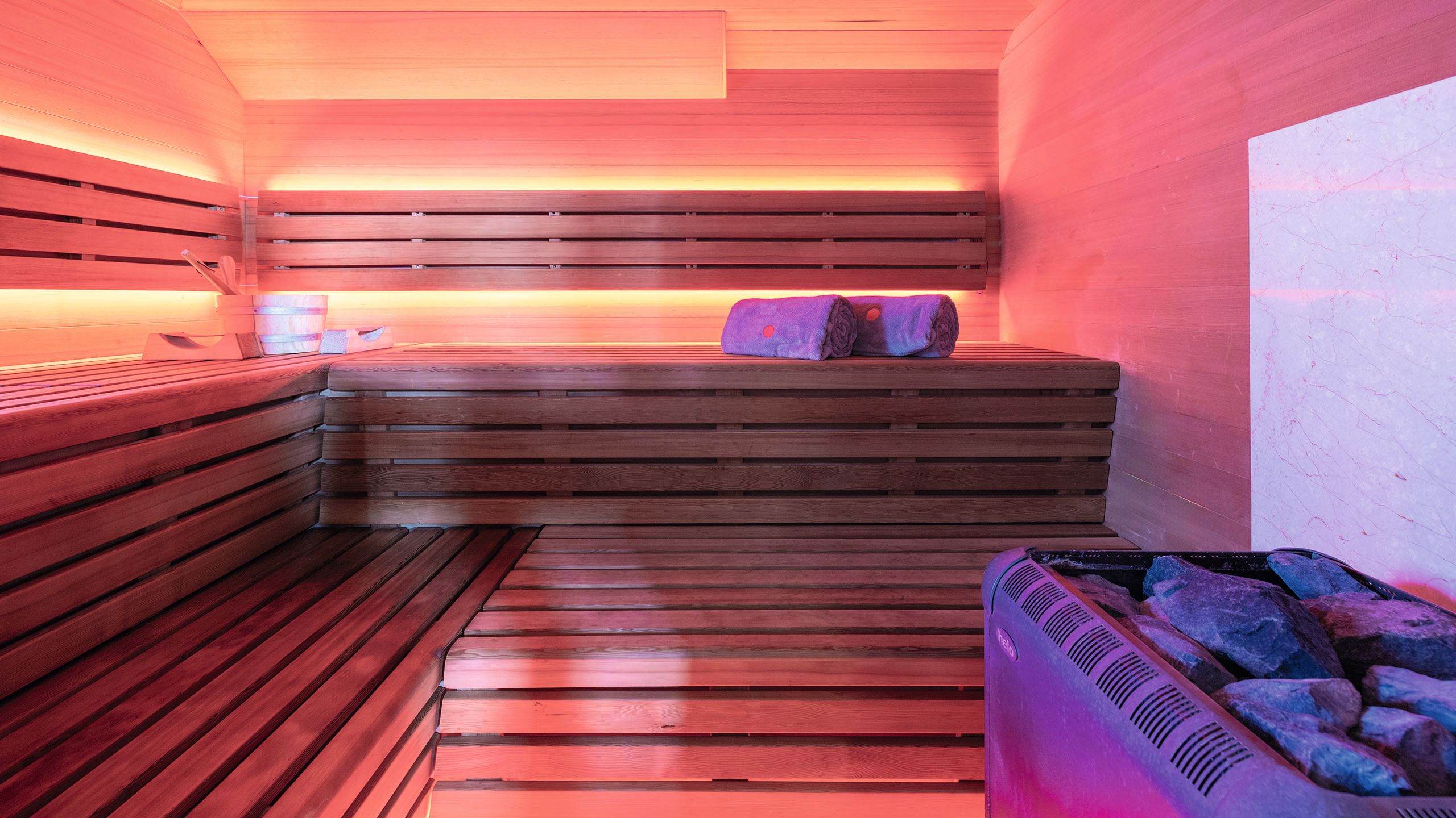Inside the sauna which is lit up red with rolled up towels on the bench