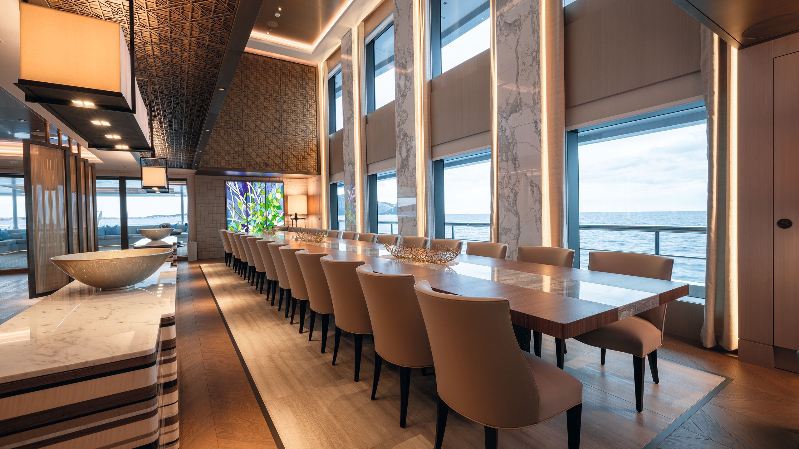 Long dining table seating 30 opposite two-storey windows on one side