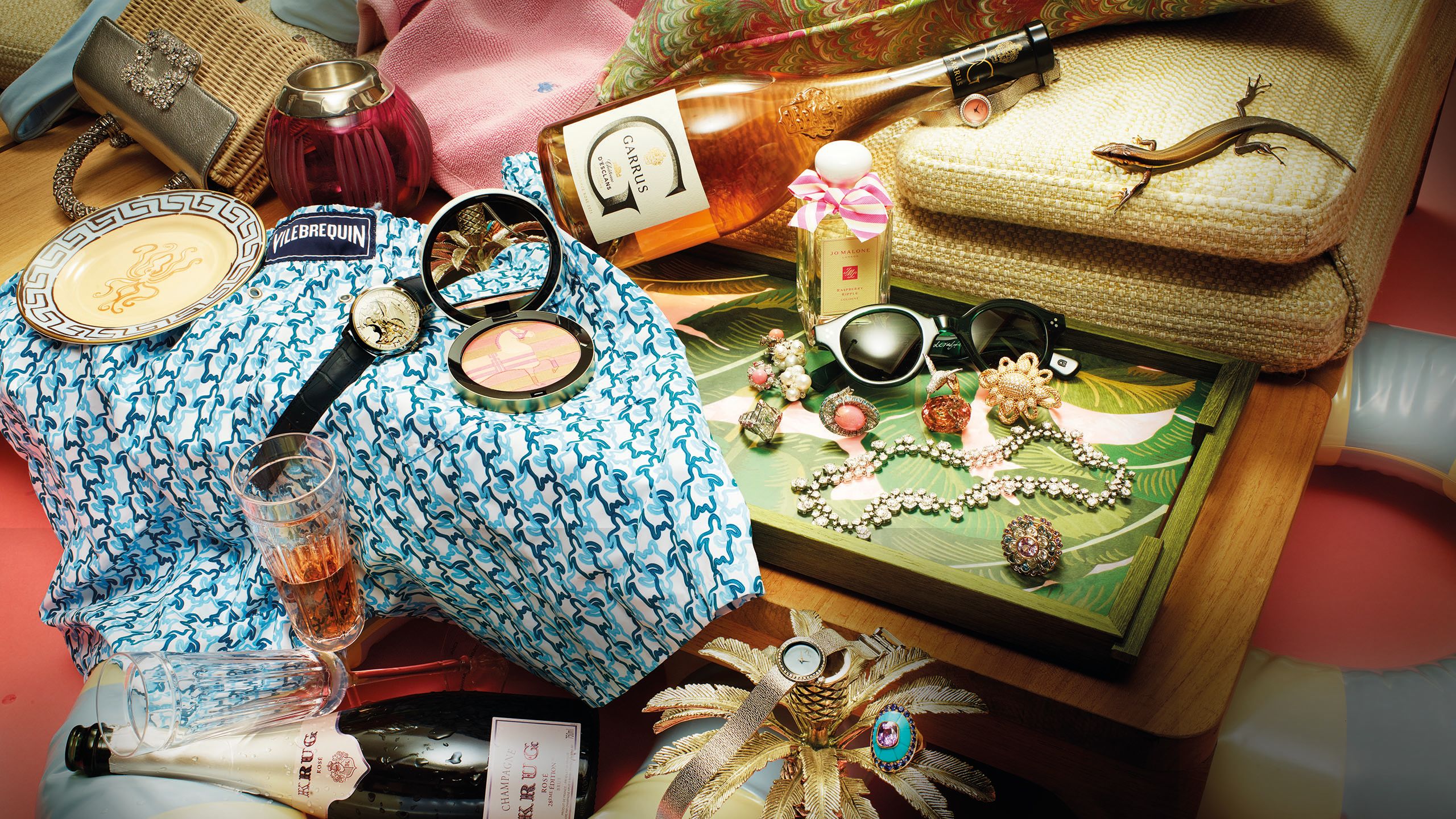 Gifts in a colonial-style palatte of green, gold pink and blue, including a bottle of Krug, palm tree candle stick, tray and maximilist rings