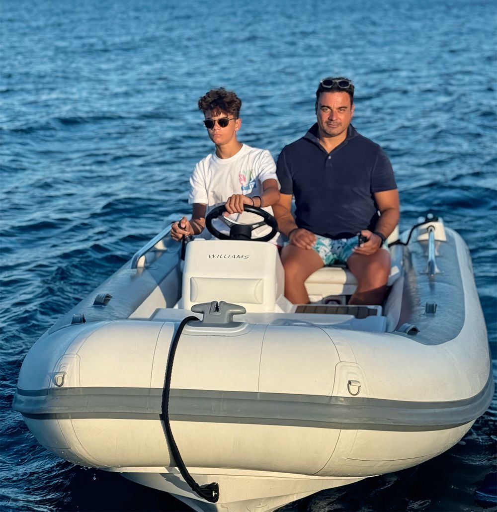 A man and a teenager at the wheel of a tender. Both are wearing short-sleeved tops