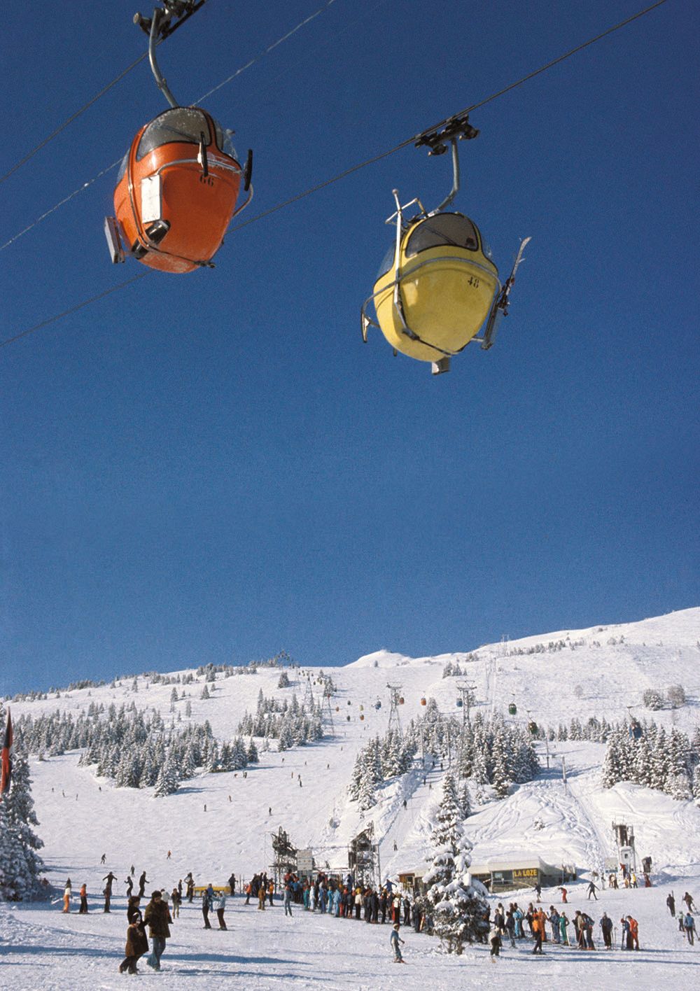 Two ski lifts, one red, one yellow, dangle over the slopes. The sky is a very deep blue