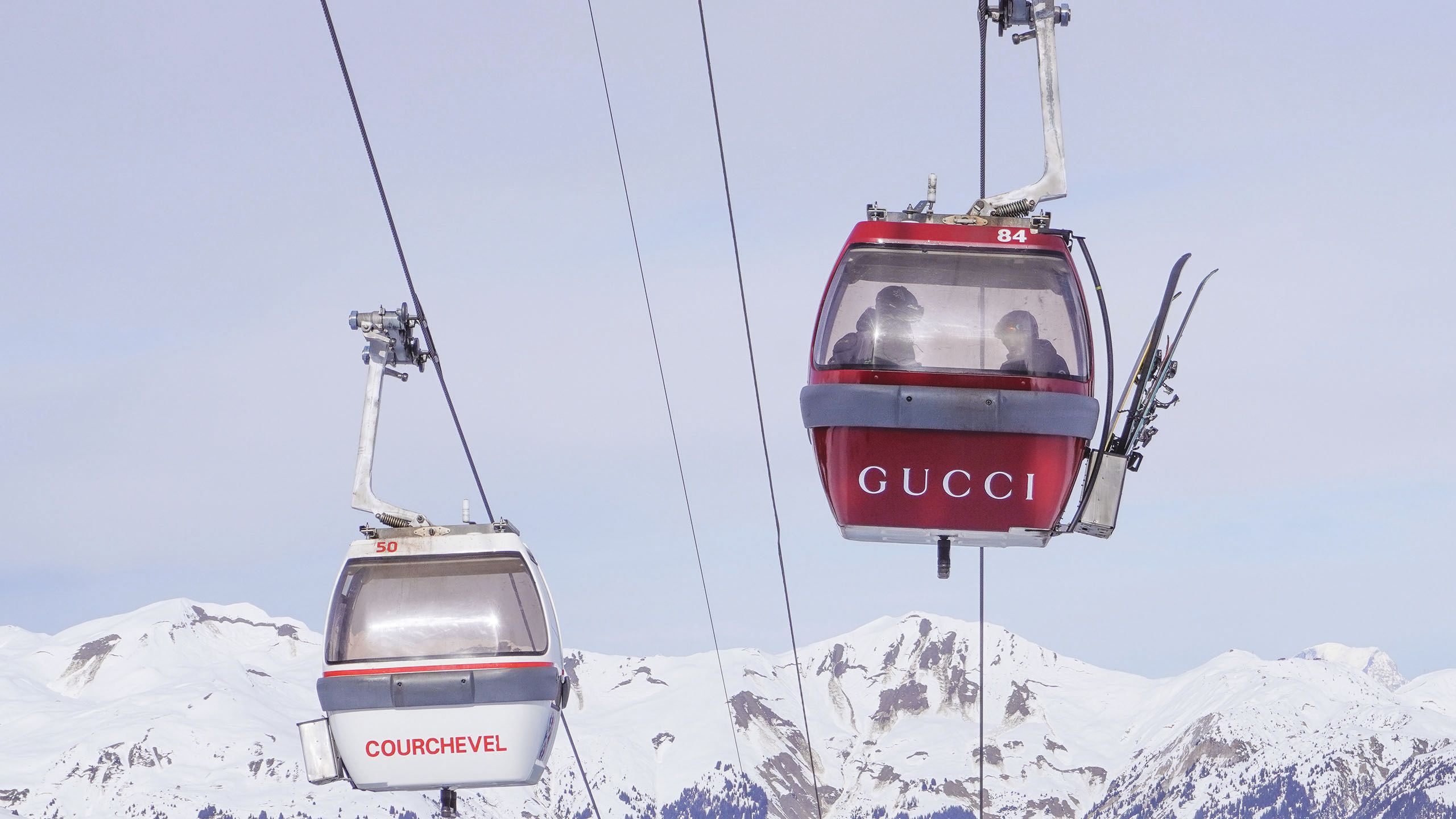 Two ski lifts, one white with the word Courchevel written in an orangey-red; the other is red with Gucci written in white