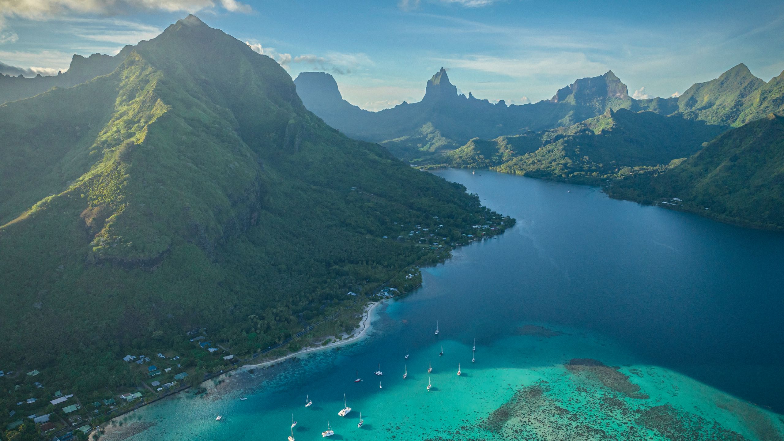 A view from the air of a mountaineous part of an island. The water is deep blue in the centre and turquoise towards the coastline