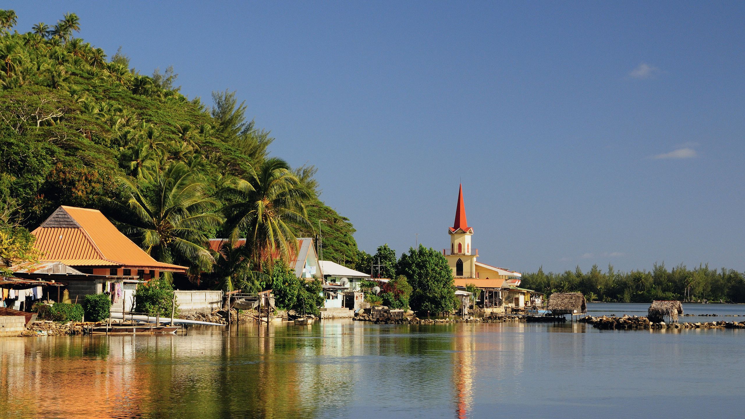 View of the shoreline which has buildings with red roofs, palm trees and in the distance, a church with a red steeple