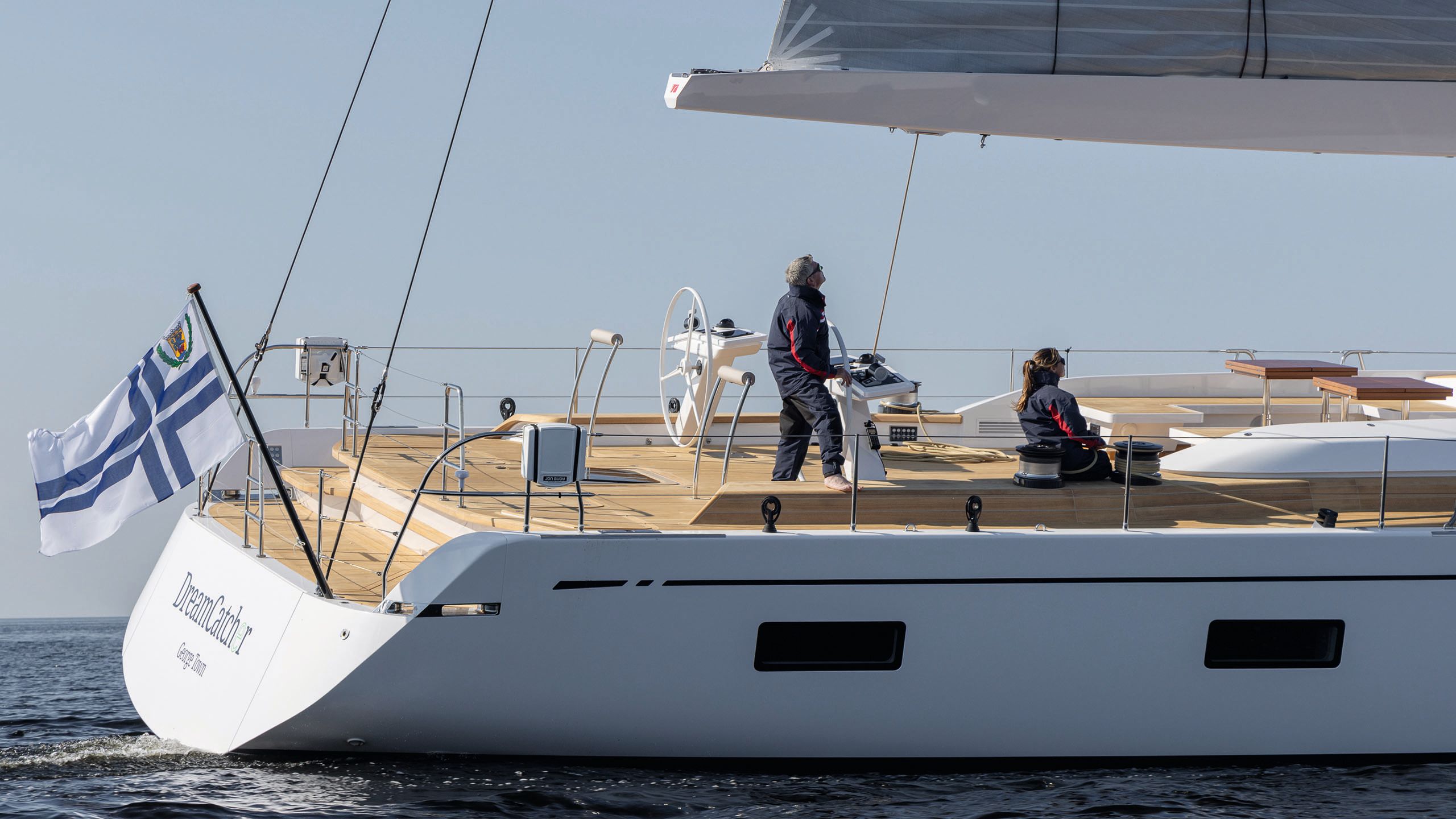 Side view of DreamCatcher on the water - two people are on the deck, one standing at a wheel and the other seated
