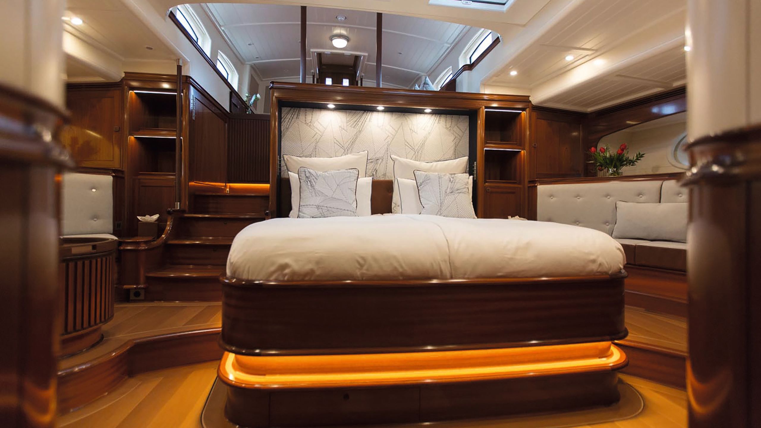 The bedroom is largely done out in mahogany wood with a large bed in the centre that is lit from beneath with orange lighting. There are white sheets and pillows.