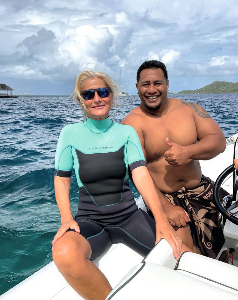 Ramona is wearing a turquoise and black wetsuit and sunglasses. The male guide is wearing a sarong and is topless - he is giving the camera a thumbs up
