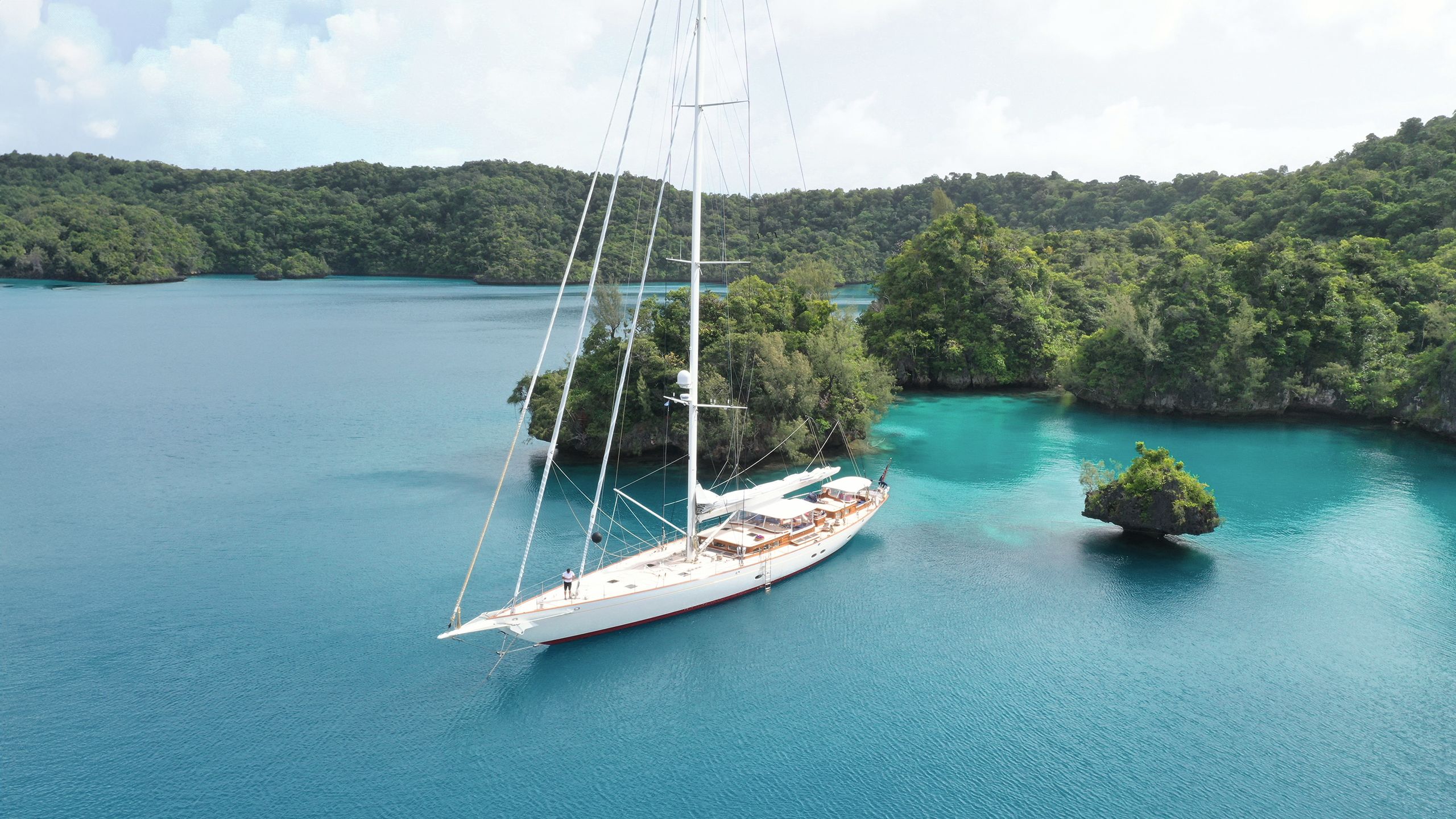 Side view of Vijonara in the South Seas - the water is turquoise and there are lush green trees at the water's edge