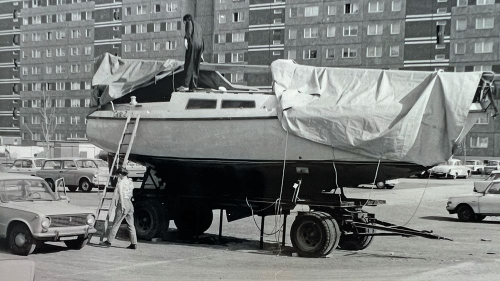 Black and white photo of the boat sitting in a car park, partially covered with a piece of material