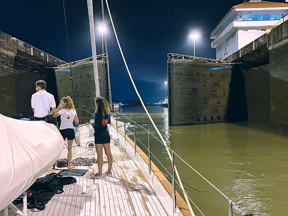 View of the boat about to pass through the canal at night. There are two girls and a man on board with their backs to the camera