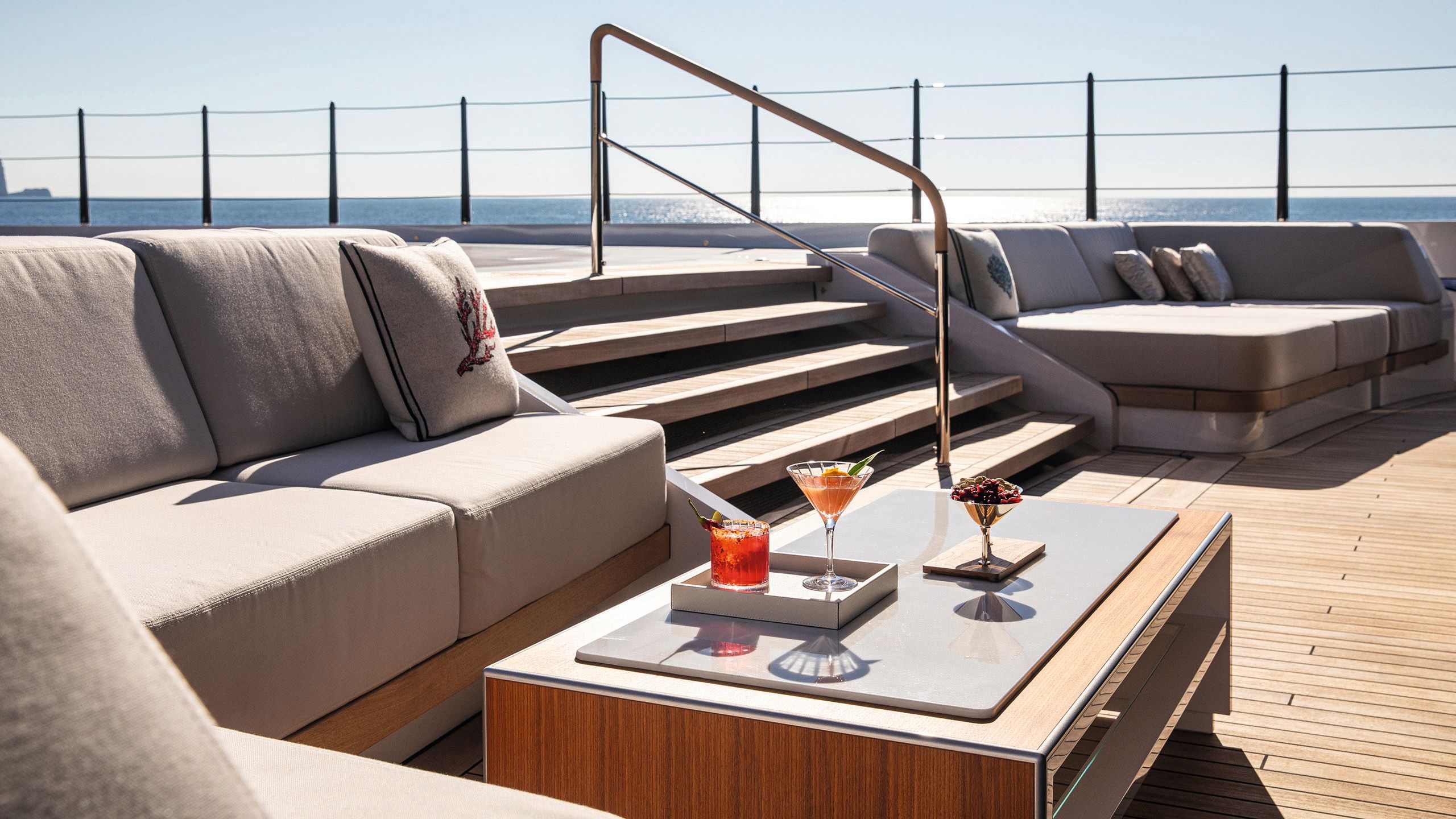 Stairs on an outdoor deck with L-shaped sofas either side and a table with cocktails on it