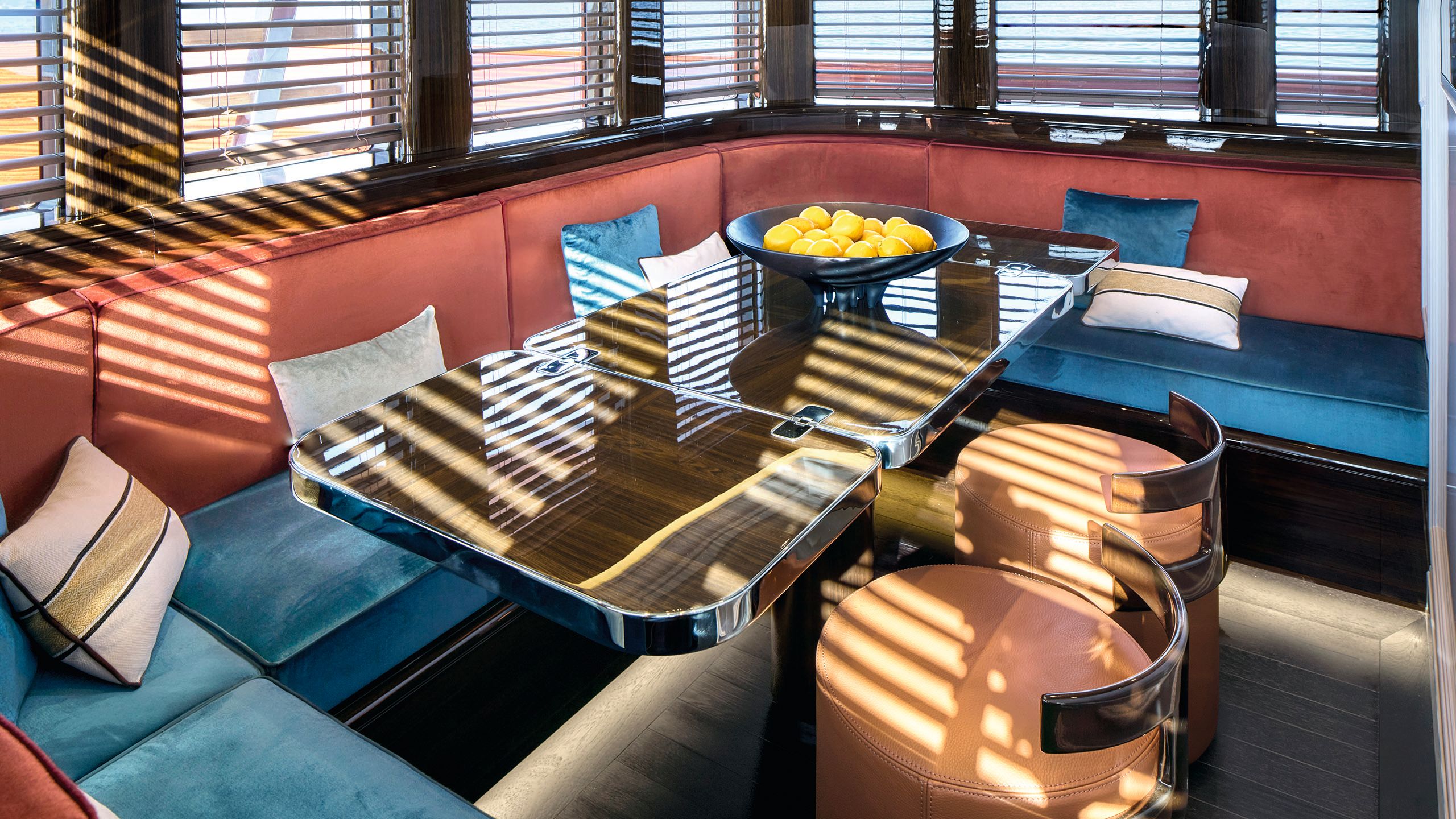 Inside dining area. The banquette seating is red and blue velvet with contrasting cushiosn. The table is cafe-style with a shiny top. There are two circular orange chairs in front