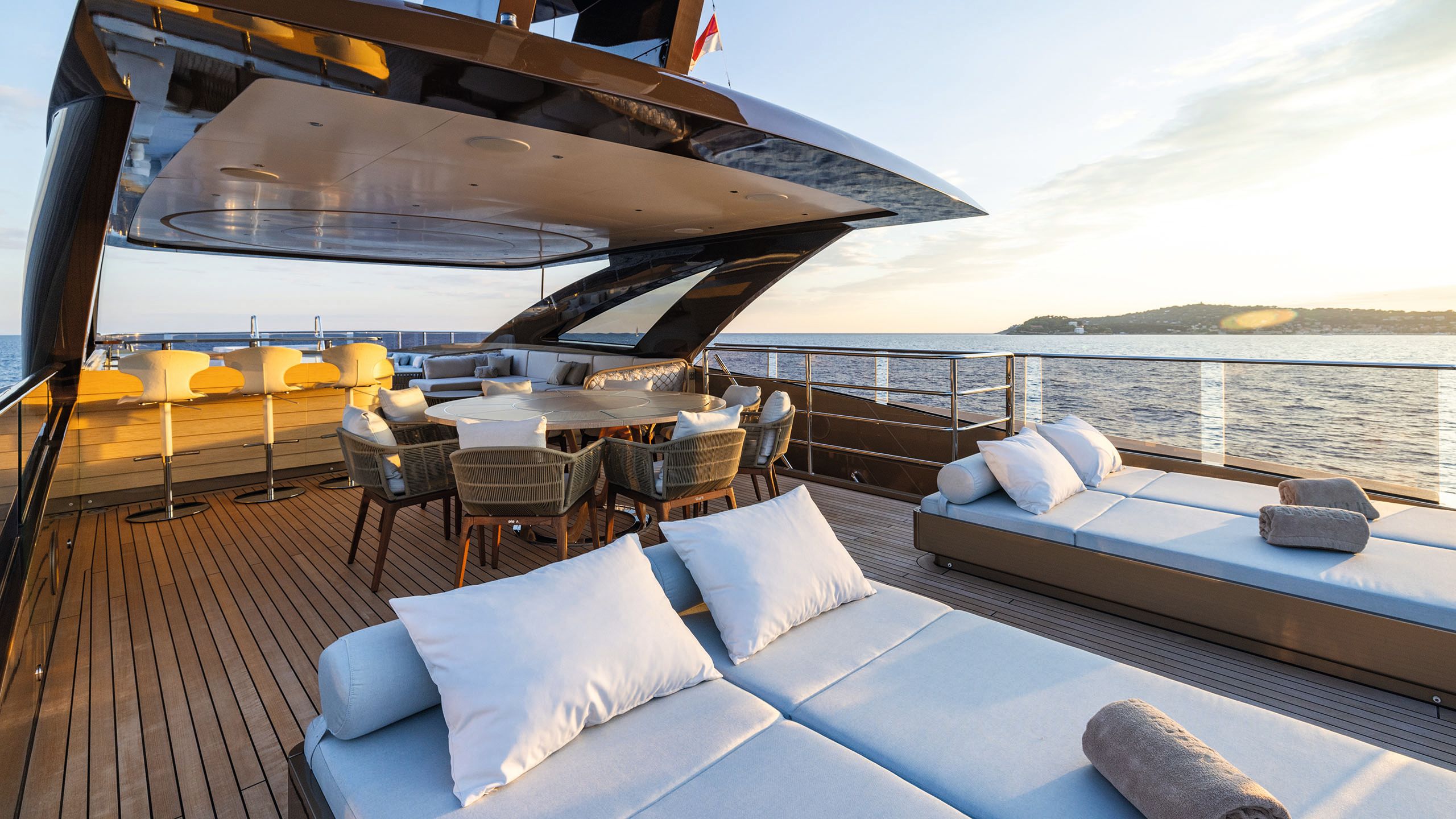 View of another deck with sunloungers in the foreground and a circular table with chairs and a bar and sofa behind