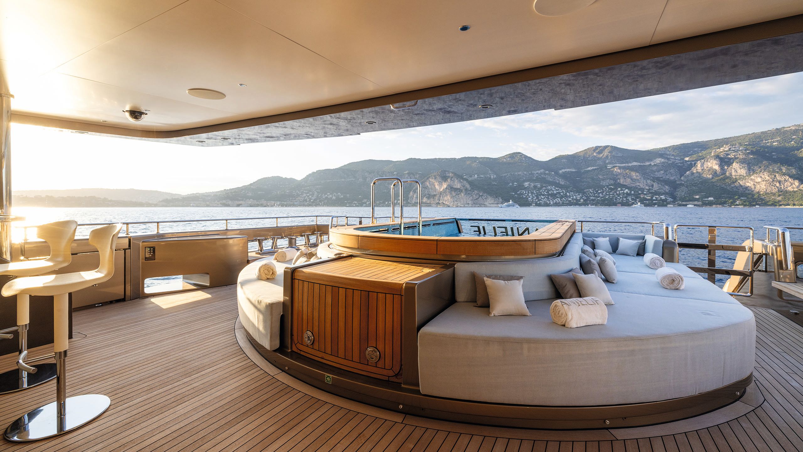 A deck with pool clad in teak with white sofas encircling it