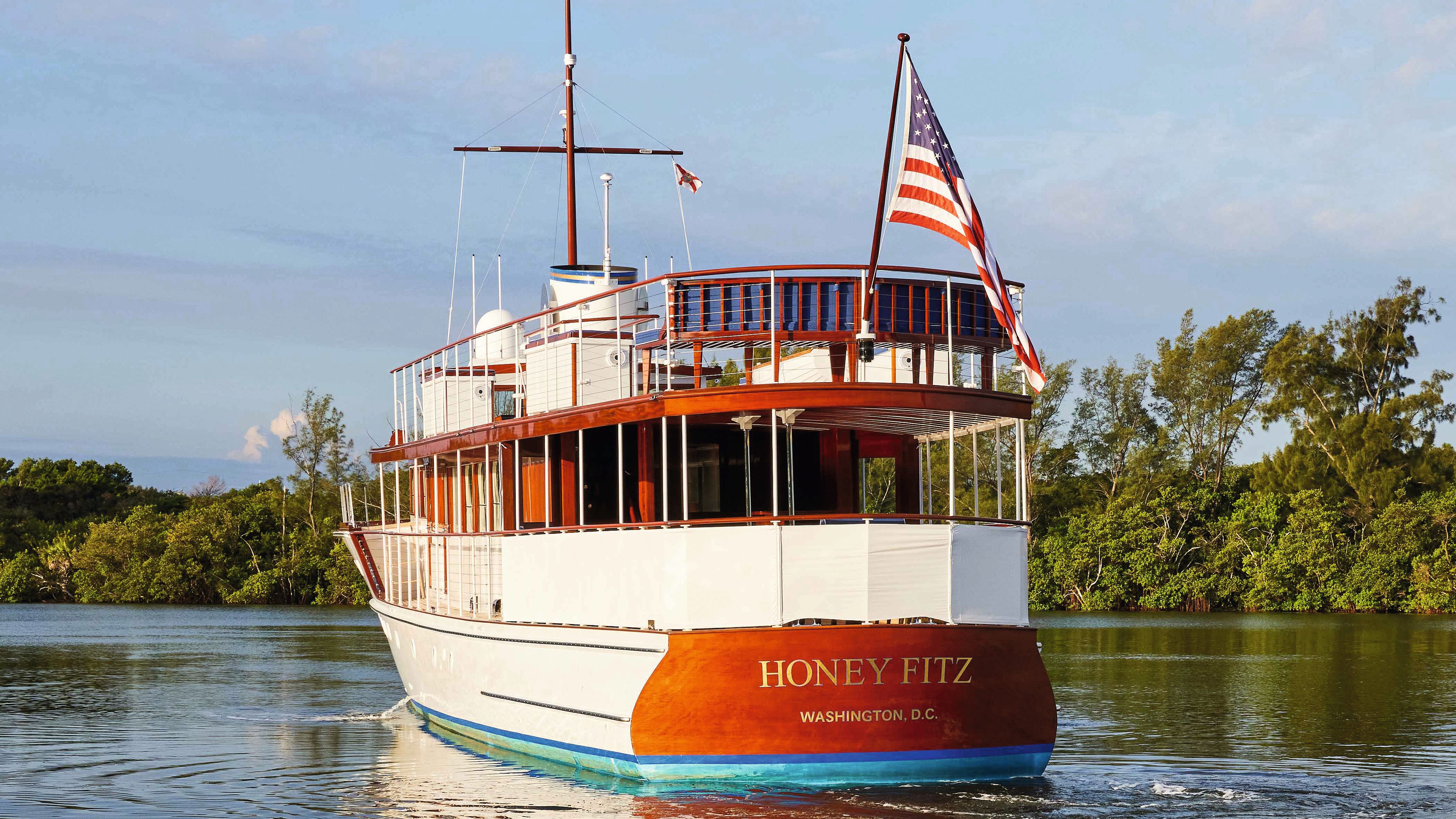 Honey Fitz from the front - she is built using teak and mahogany and is partially white. There are railings all round the sides and a US flag at the front 