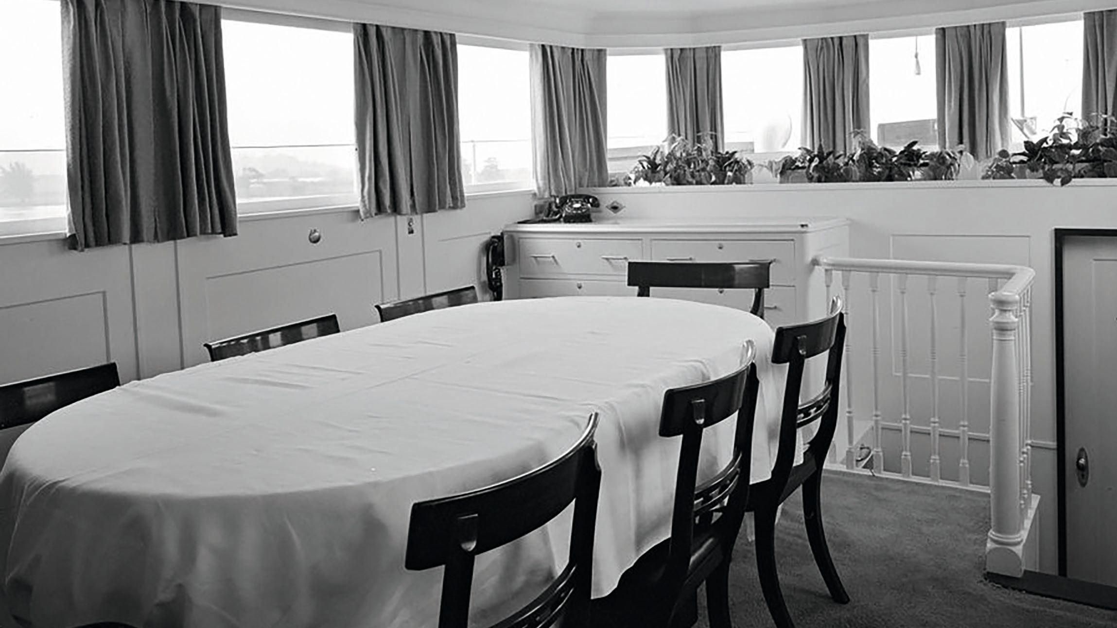 A black and white snapshot of the dining room taken in 1961. There's a large oval table in the centre and seven chairs