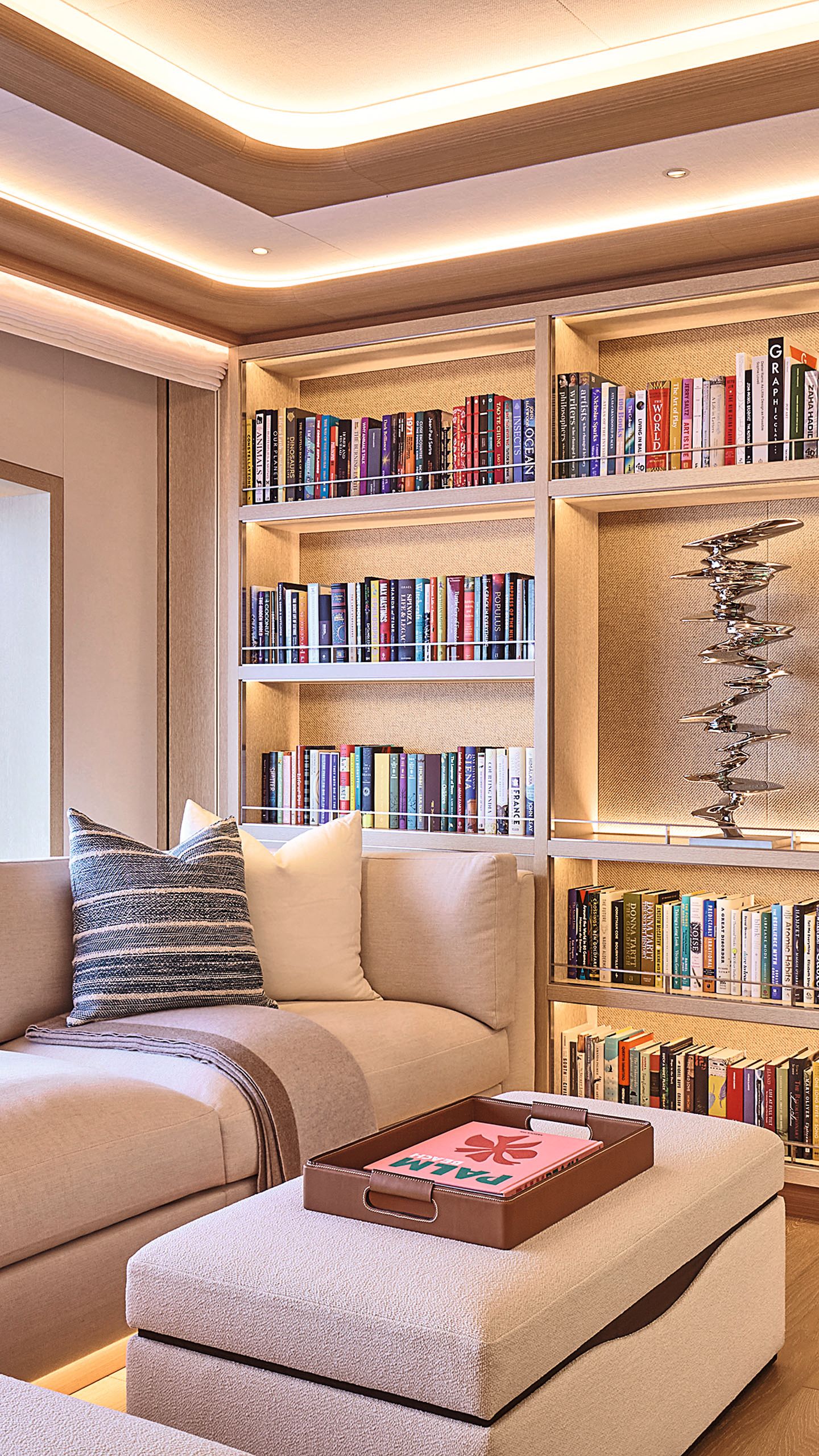 Books on shelves with a sofa and footstool in foreground