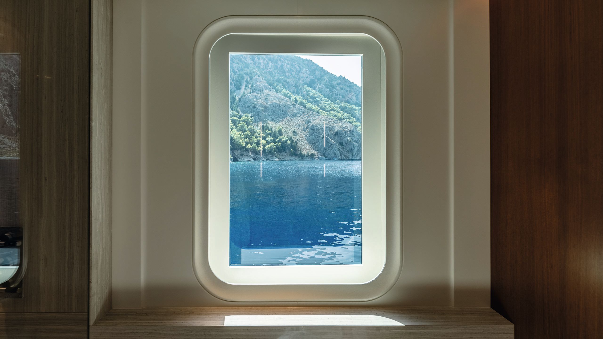 A rectangular window with white surround looking out on to blue waters and mountains in the background
