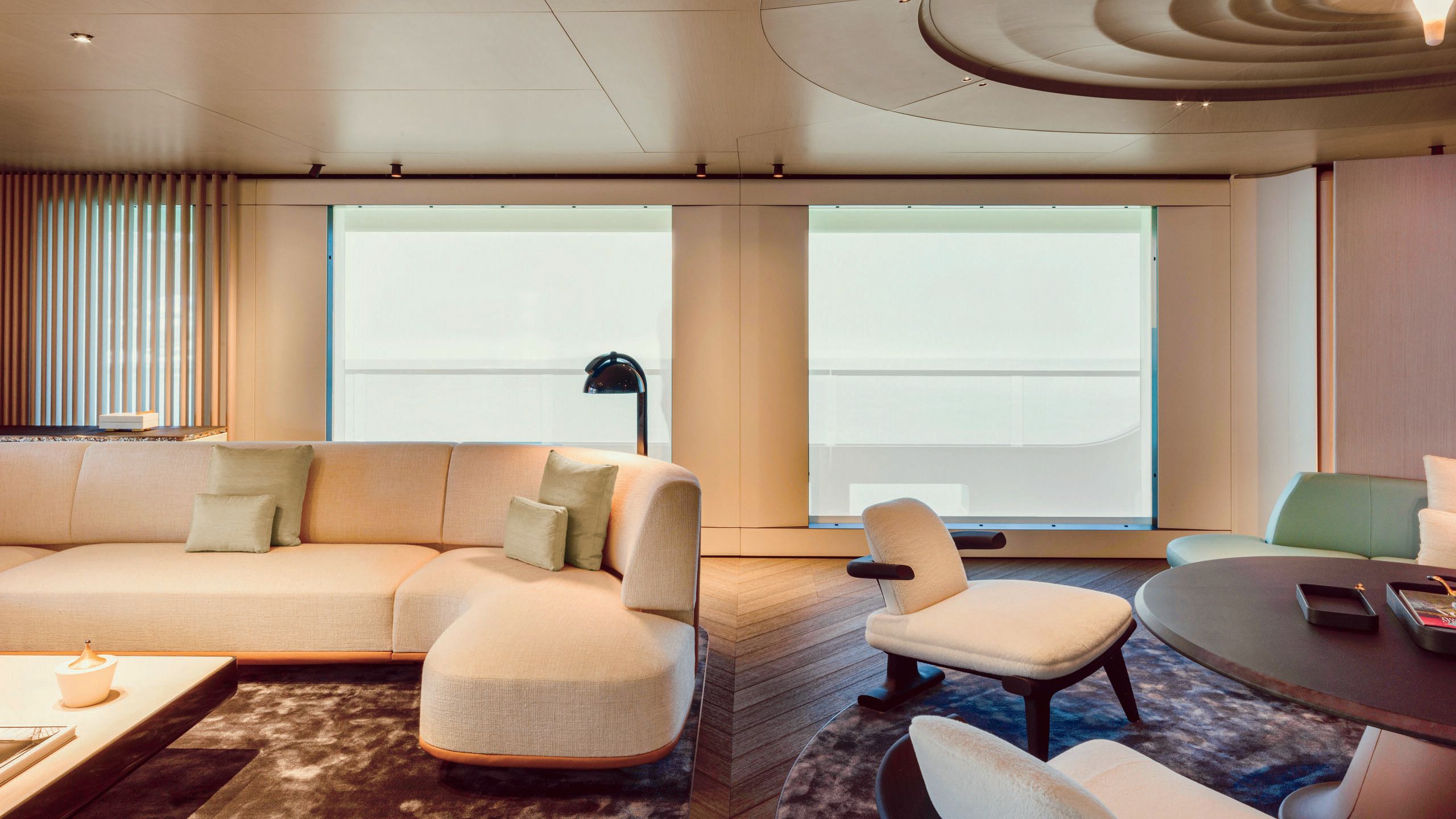 Large L-shaped sofa in cream to the left and low-slung, matching armchairs around a dark brown circular table to the right