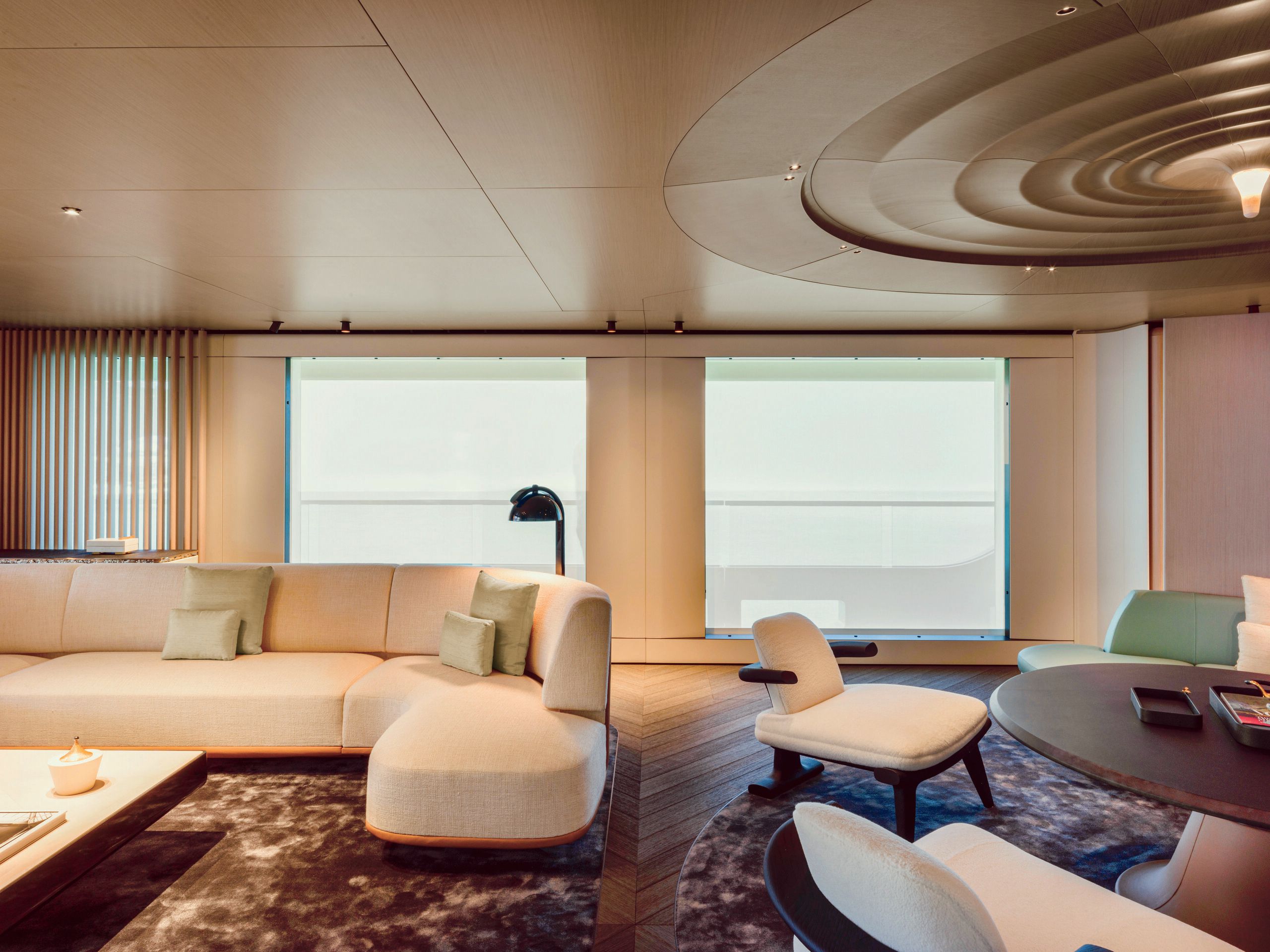 Large L-shaped sofa in cream to the left and low-slung, matching armchairs around a dark brown circular table to the right