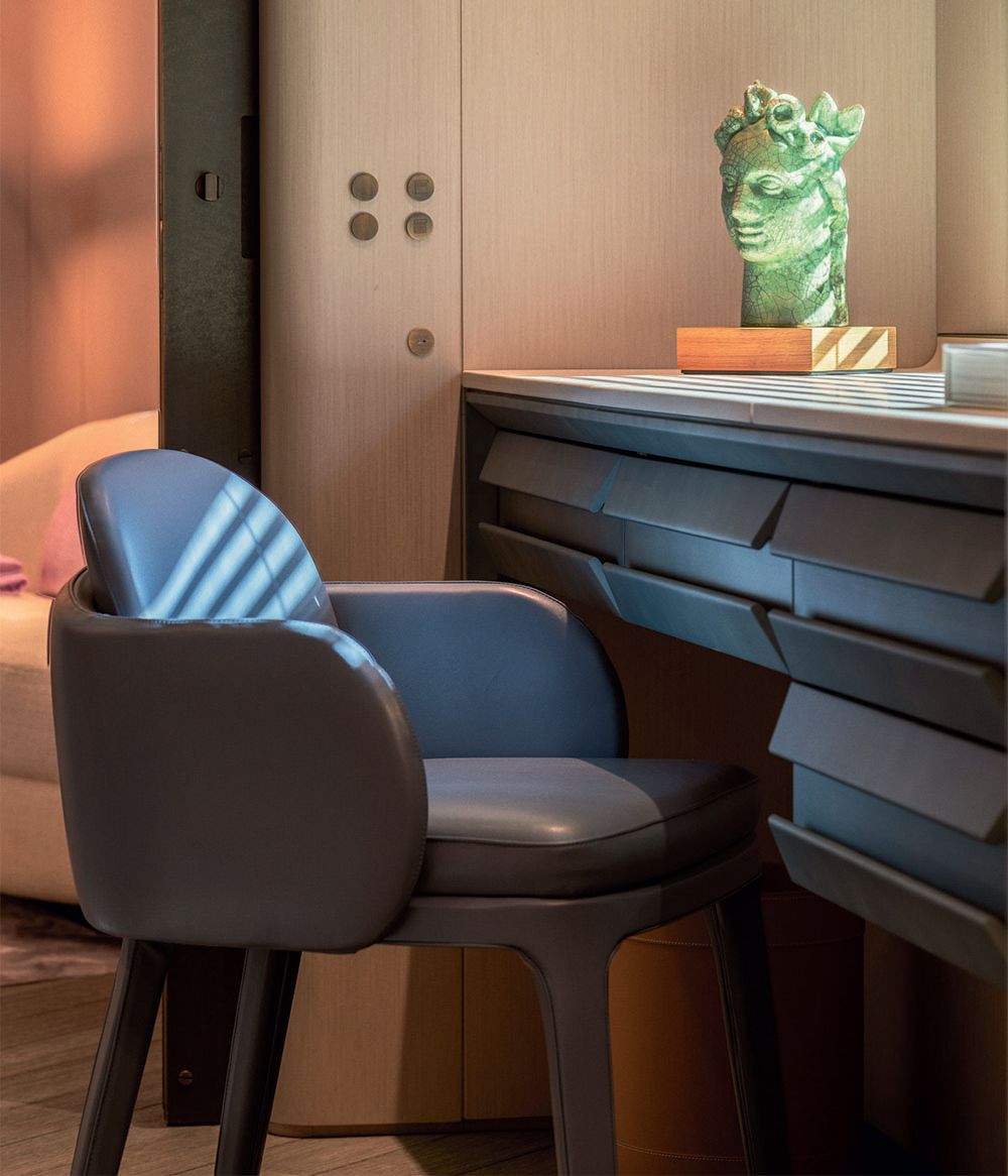 A dark blue desk and chair with small green bust on a wooden block