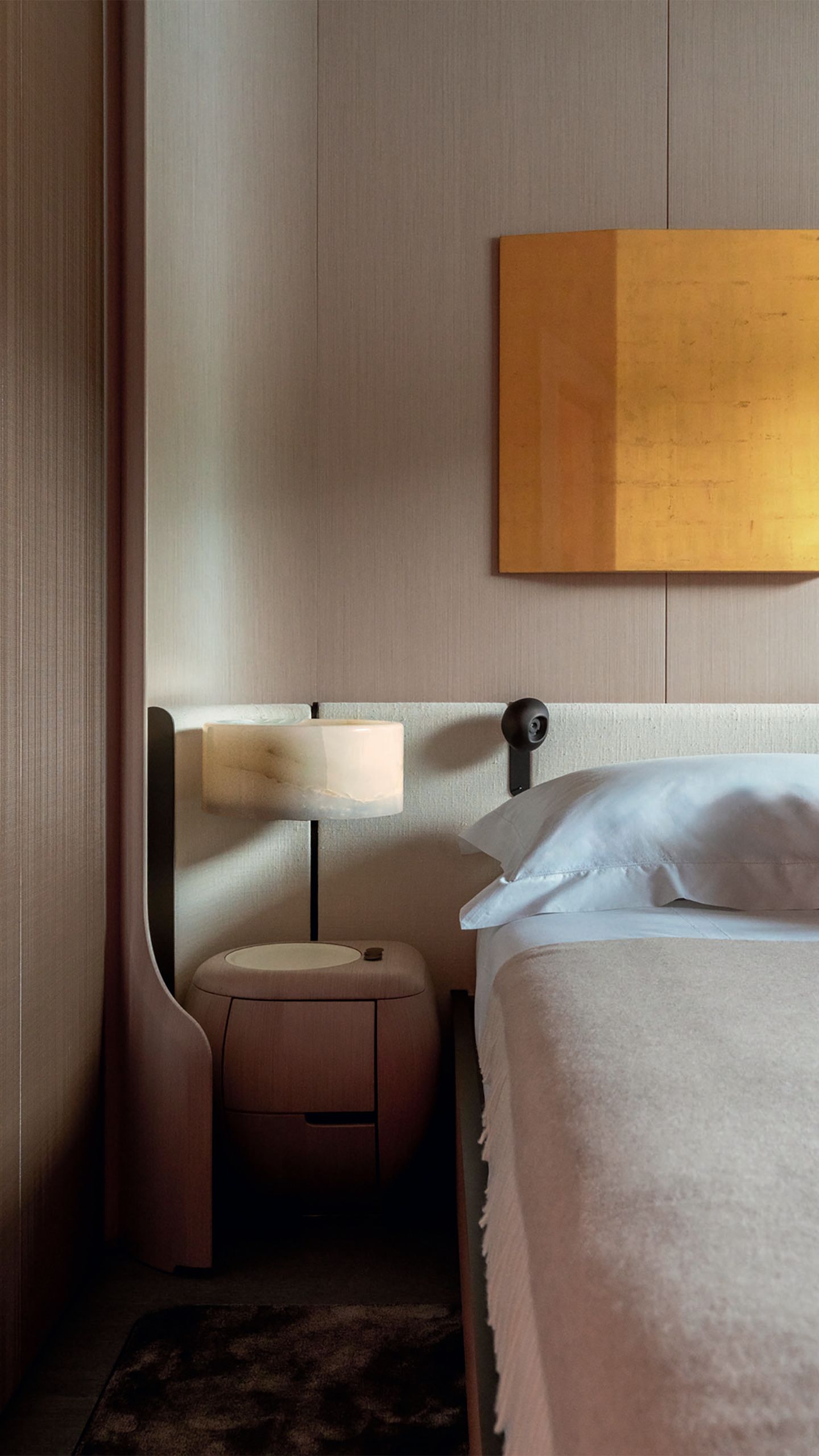 Looking down the side of a bed with curved headboard and small curved lamp