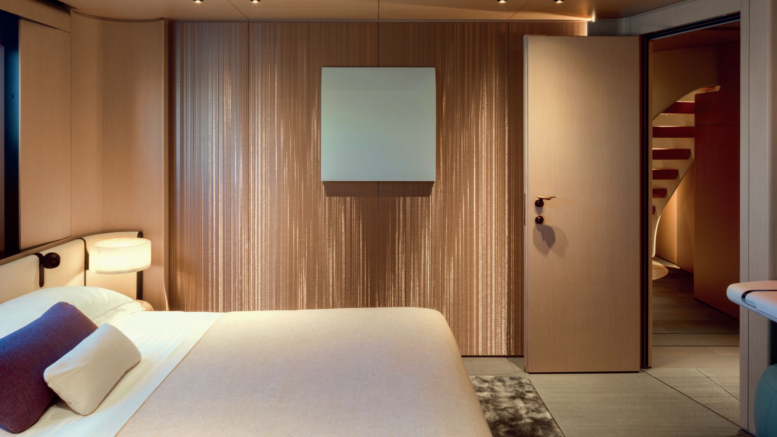 Side view of a guest bedroom. The bed is made up in neutral linens with accent purple cushion