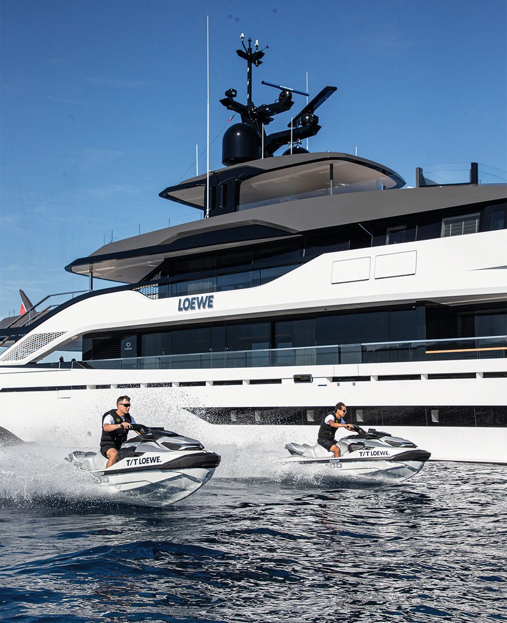 Side view of Loewe on the water. Two men are on tenders alongside