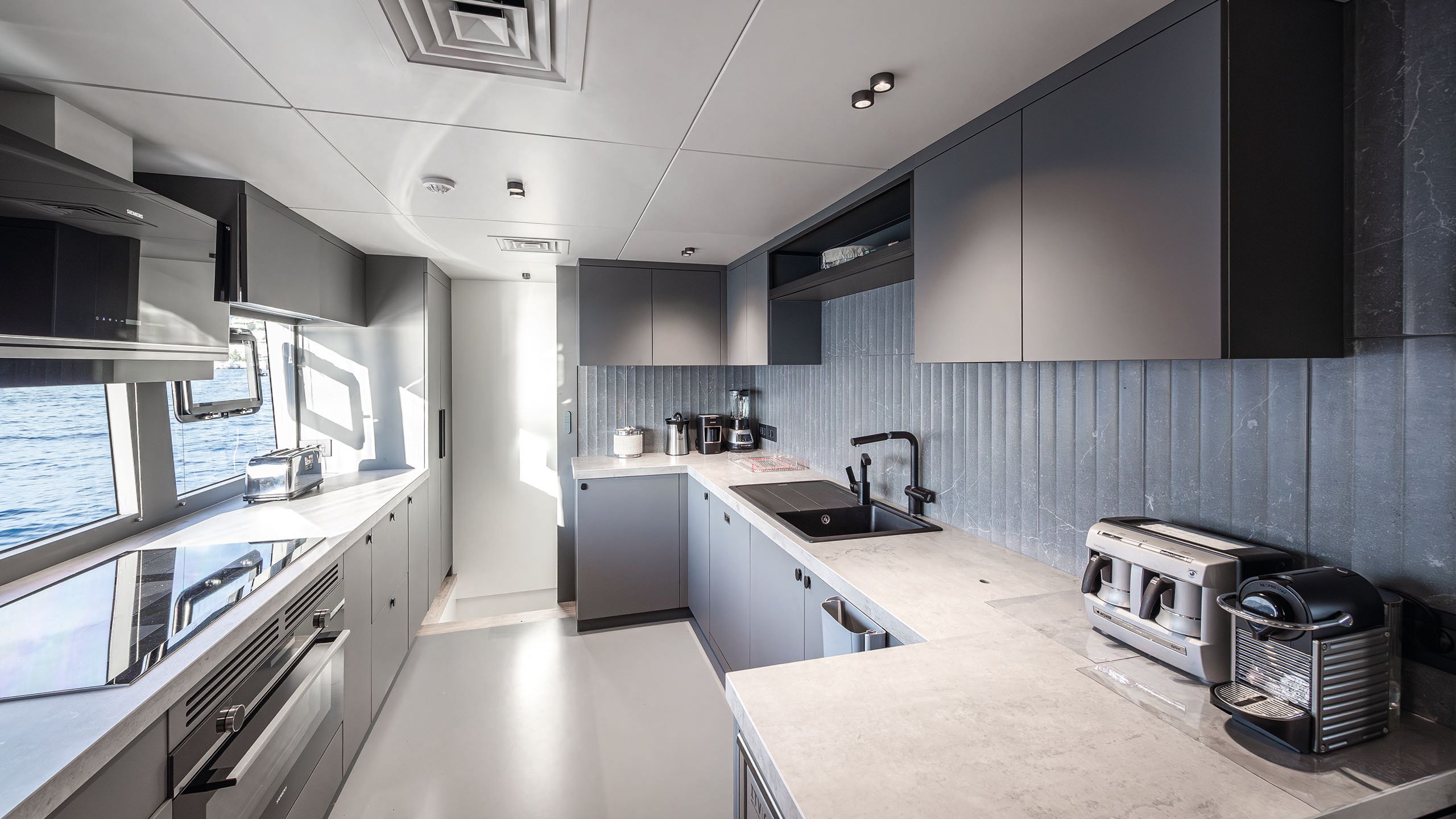 Light and airy kitchen area with grey cupboards, white counters and blue backsplash