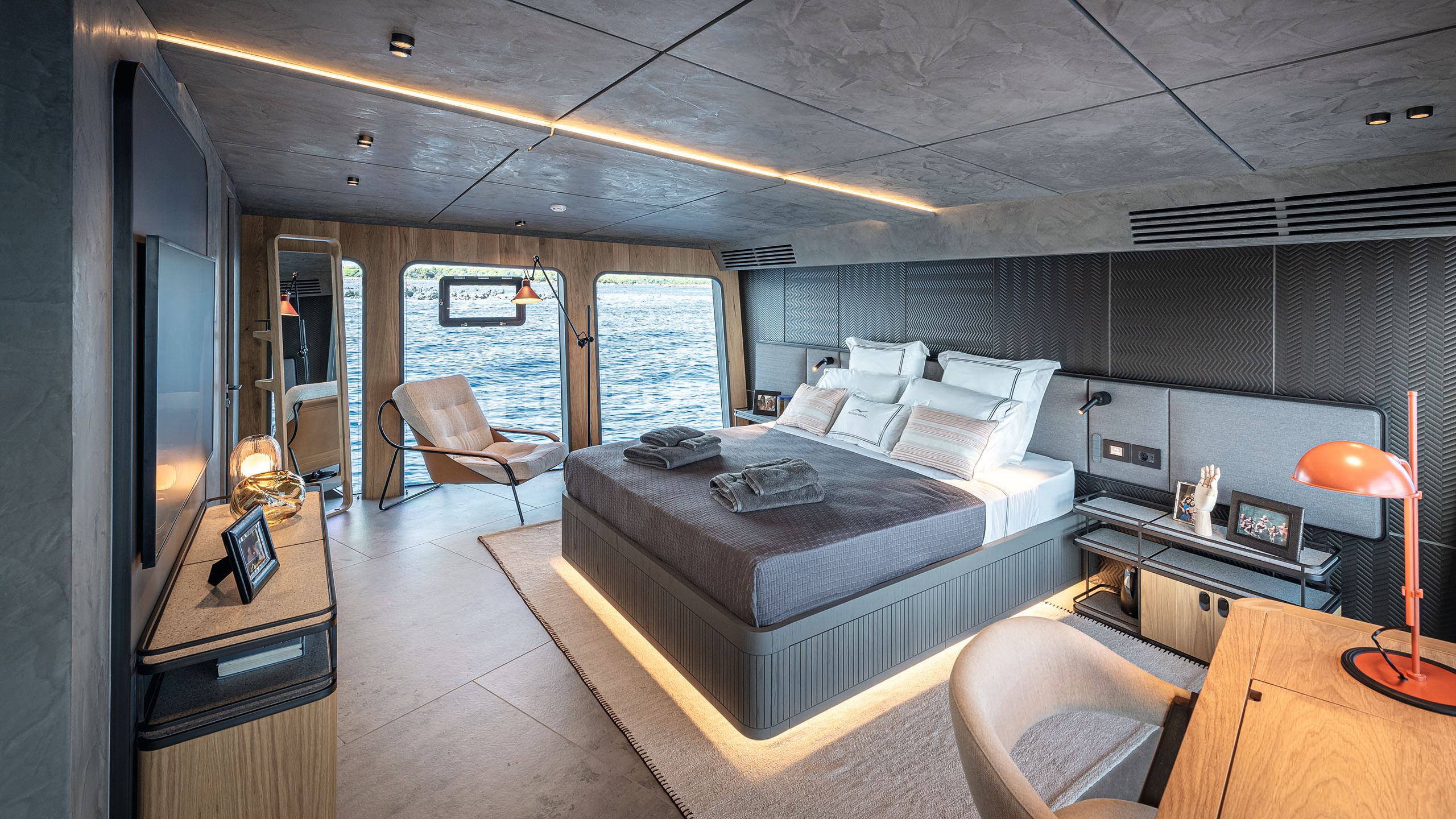 Large bed in the centre of the main cabin. The decor and ben linens are dark grey with white pillows and modern furnishings