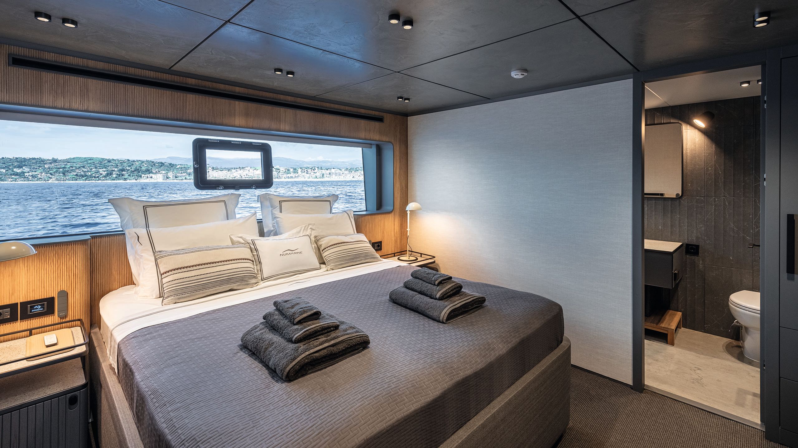 Guest cabin with bed at the centre with grey and white linens and towels