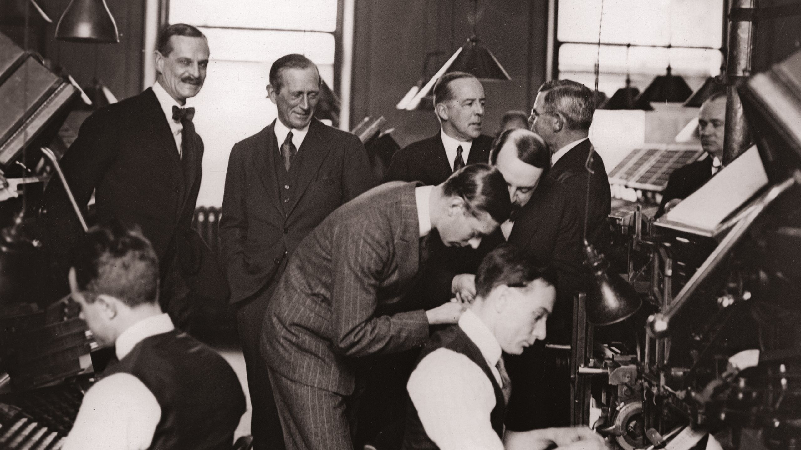 Black and white photo of men in suits inside a newspaper office