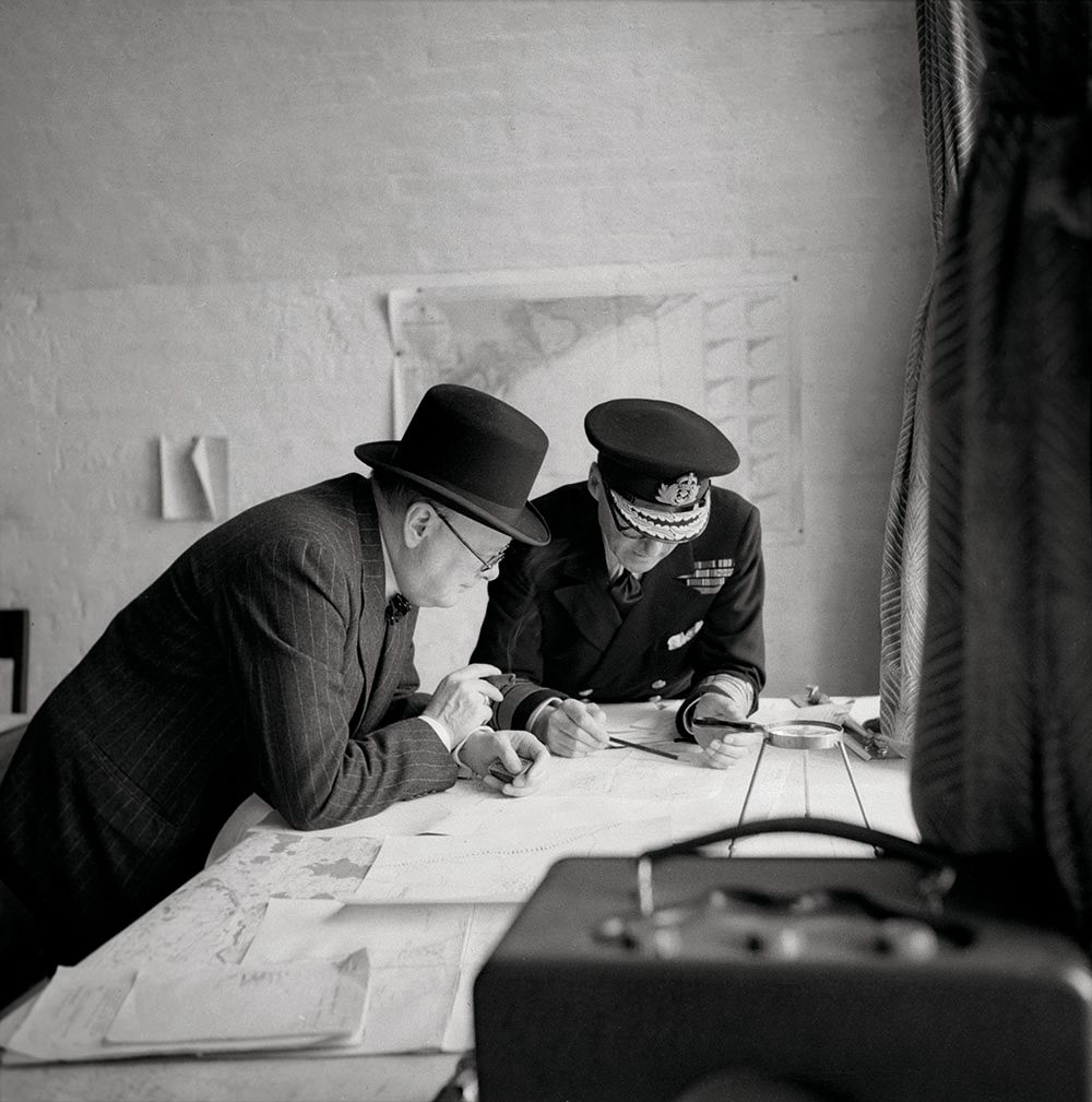 Black and white photo of Churchill and Ramsay leaning over papers 